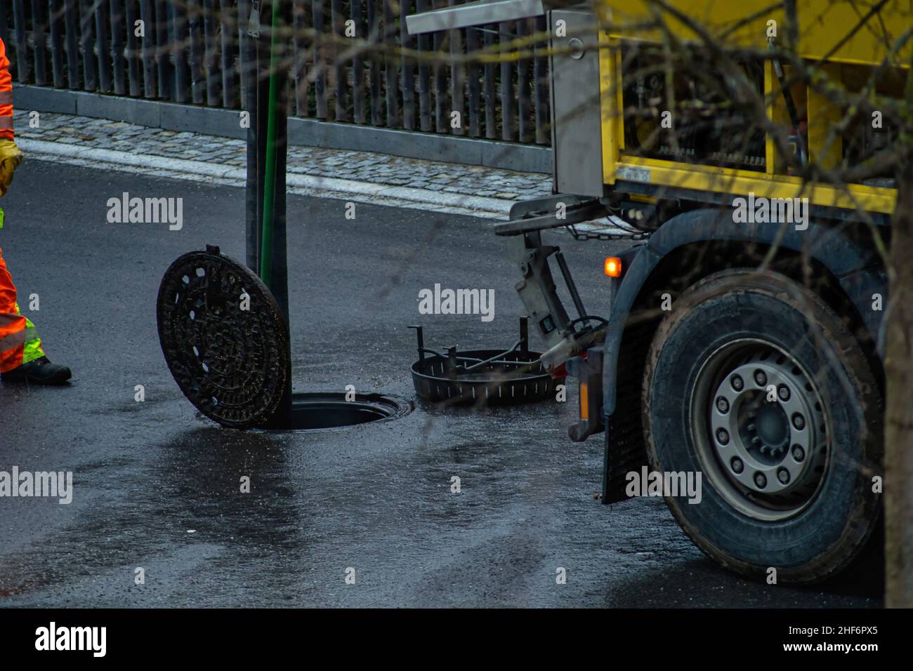 Scolamento che pulisce il lavoratore è in piedi di fronte ad una copertura aperta del tombino, facendo il suo lavoro ad un giorno piovoso su una strada Foto Stock