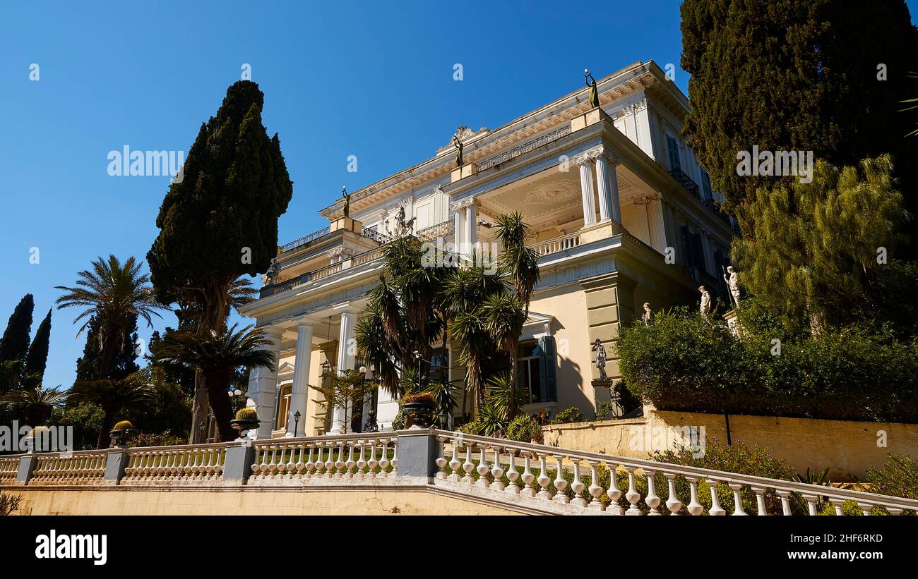 Grecia, Isole greche, Isole IONIE, Corfù, Achilleion, residenza dell'imperatrice Sissis, costruita nel 1889, architettura basata sulla mitologia greca, vista grandangolare, fronte completo dell'Achilleion, diagonalmente dal basso a destra, alberi a sinistra e a destra, cielo blu Foto Stock