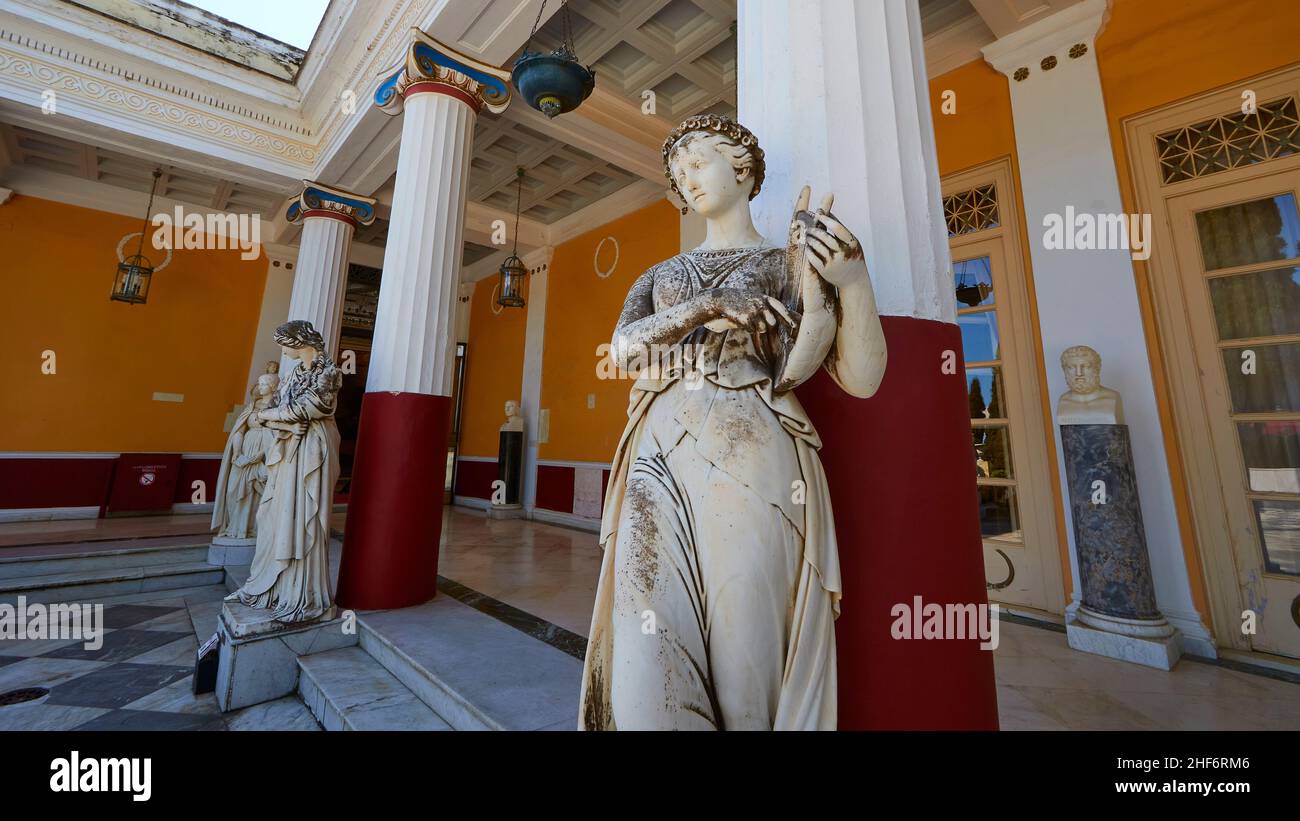 Grecia, Isole greche, Isole IONIE, Corfù, Achilleion, residenza imperatrice Sissis, costruita nel 1889, architettura basata sulla mitologia greca, terrazza, vista grandangolare, diagonalmente dal basso, tre colonne rosse e bianche, di fronte a essa tre delle nove muse, la musa nel primo piano sta suonando uno strumento arpa-come Foto Stock