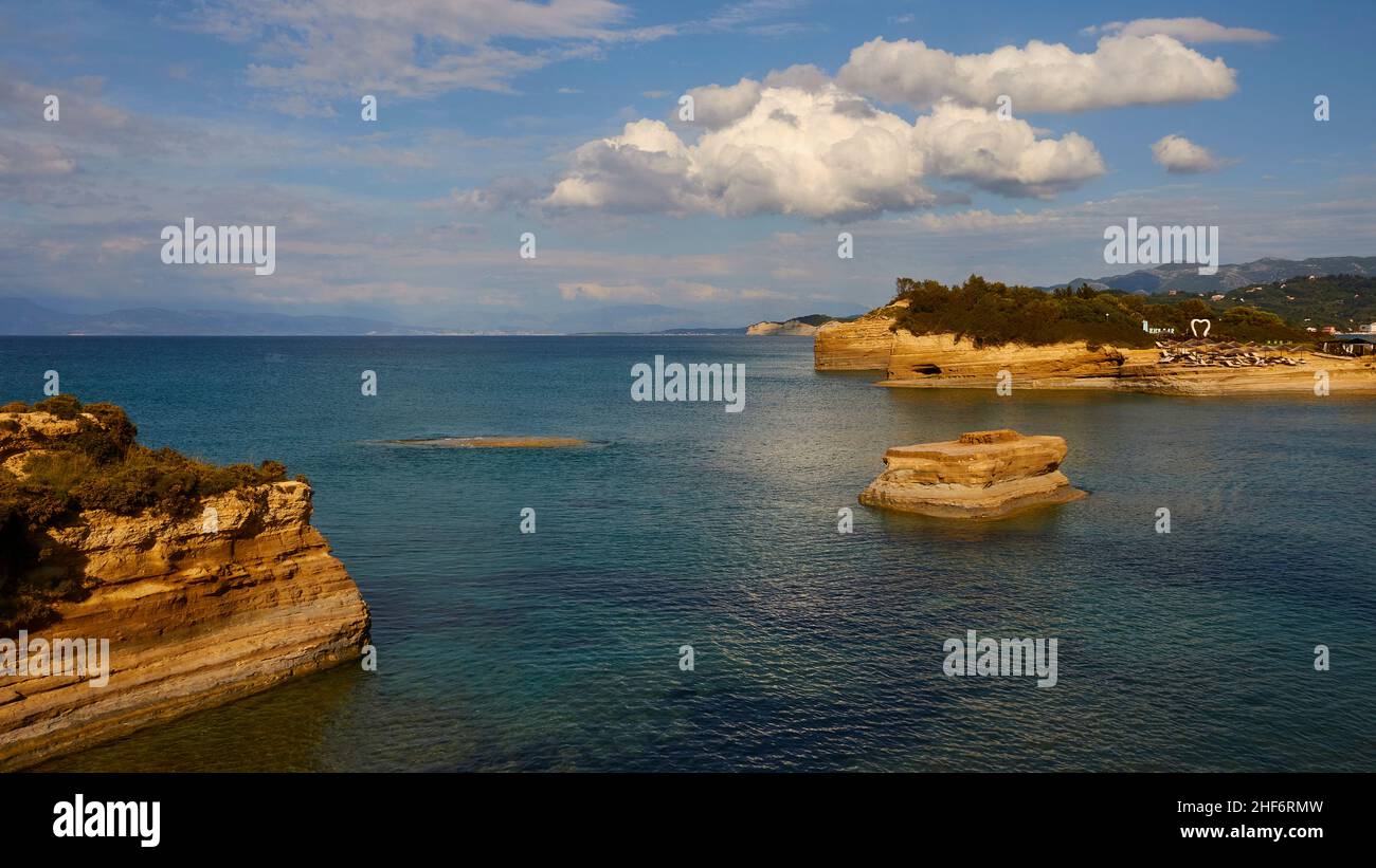 Grecia, Isole greche, Isole IONIE, Corfù, costa settentrionale, Bizzarre formazioni rocciose sulla costa, Canal d'amour, cielo blu, nuvole bianche, mare turchese, blu e verde, rocce a sinistra, isolotti di roccia al centro a destra, più costa rocciosa sullo sfondo Foto Stock