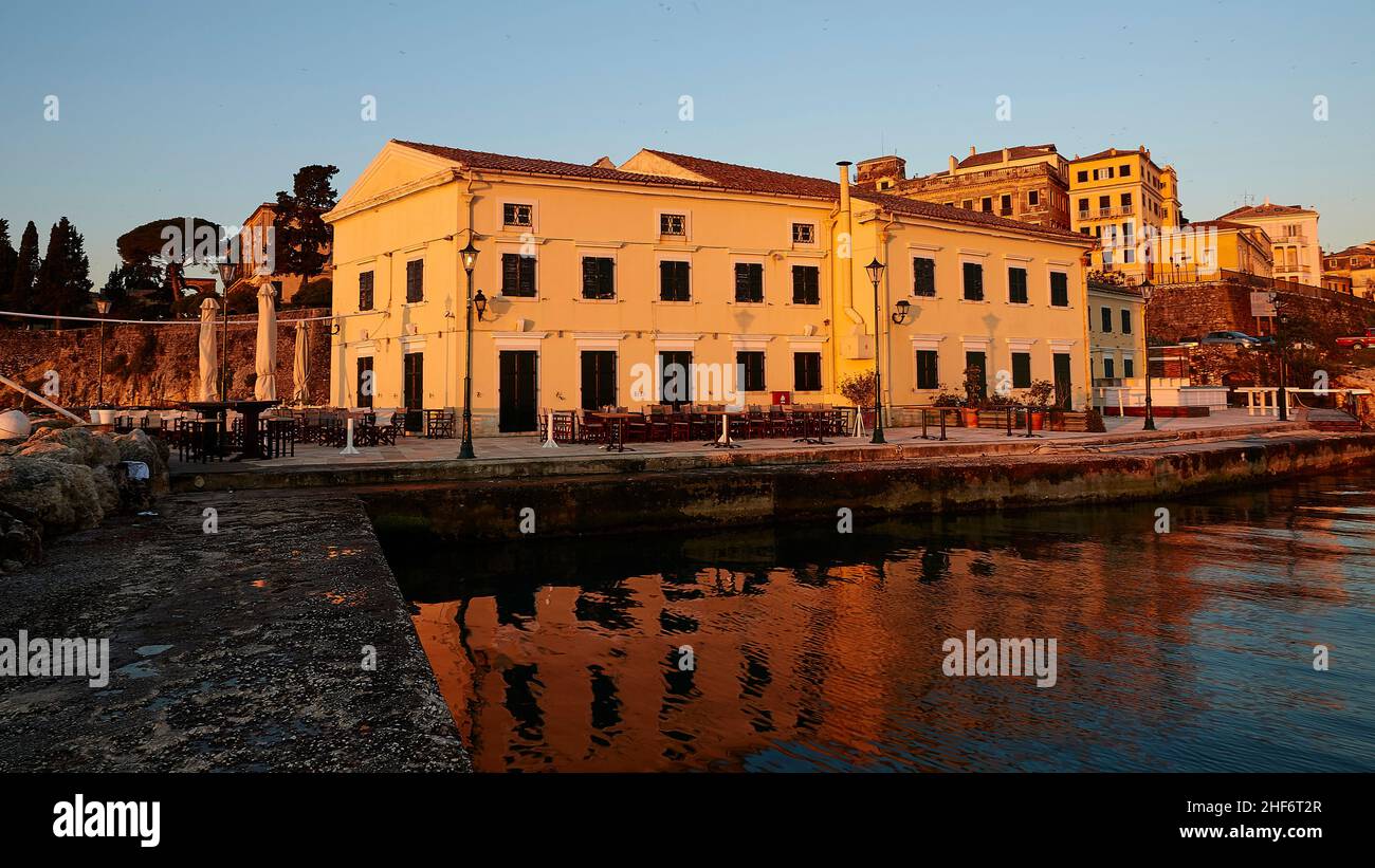 Grecia, Isole greche, Isole IONIE, Corfù, Corfù, alba sul mare, edifici sul mare alla luce del mattino, caffè, riflesso dell'edificio nel mare calmo, cielo blu Foto Stock