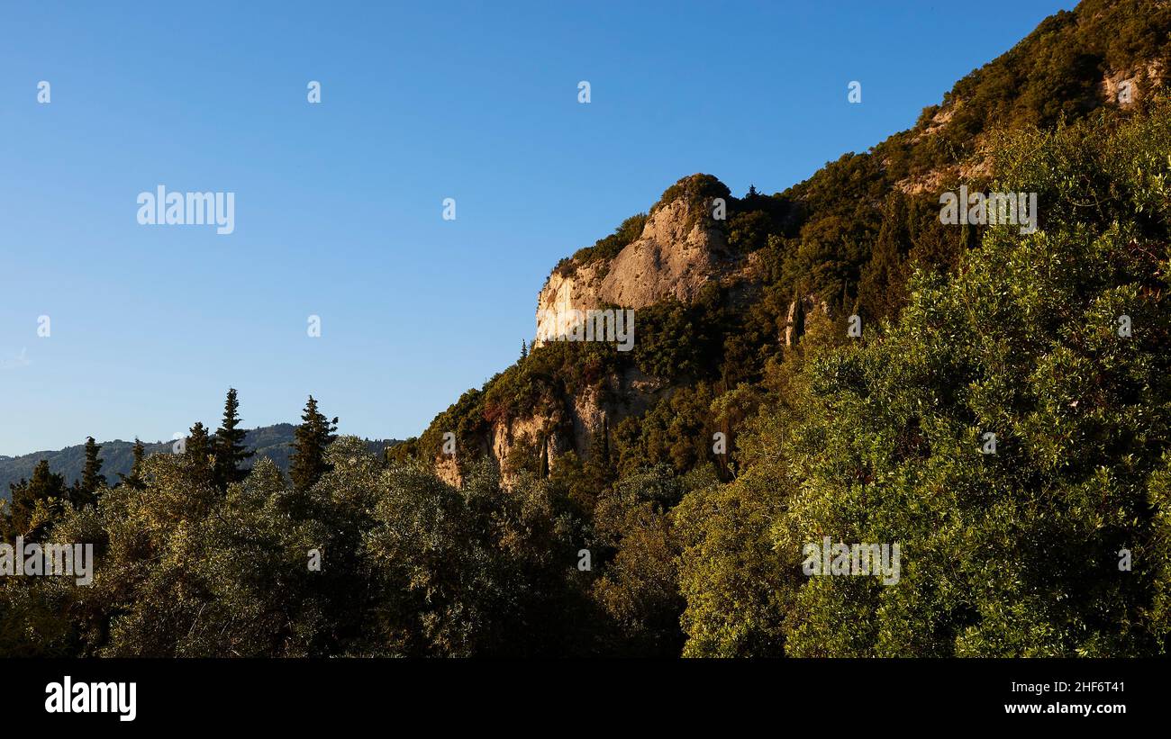 Grecia, Isole greche, Isole IONIE, Corfù, costa occidentale, Pentati, luce del pomeriggio, percorso da Pentati ad Agios Gordios, vista della roccia su un pendio, color ocra, tra cui alberi, cielo blu Foto Stock