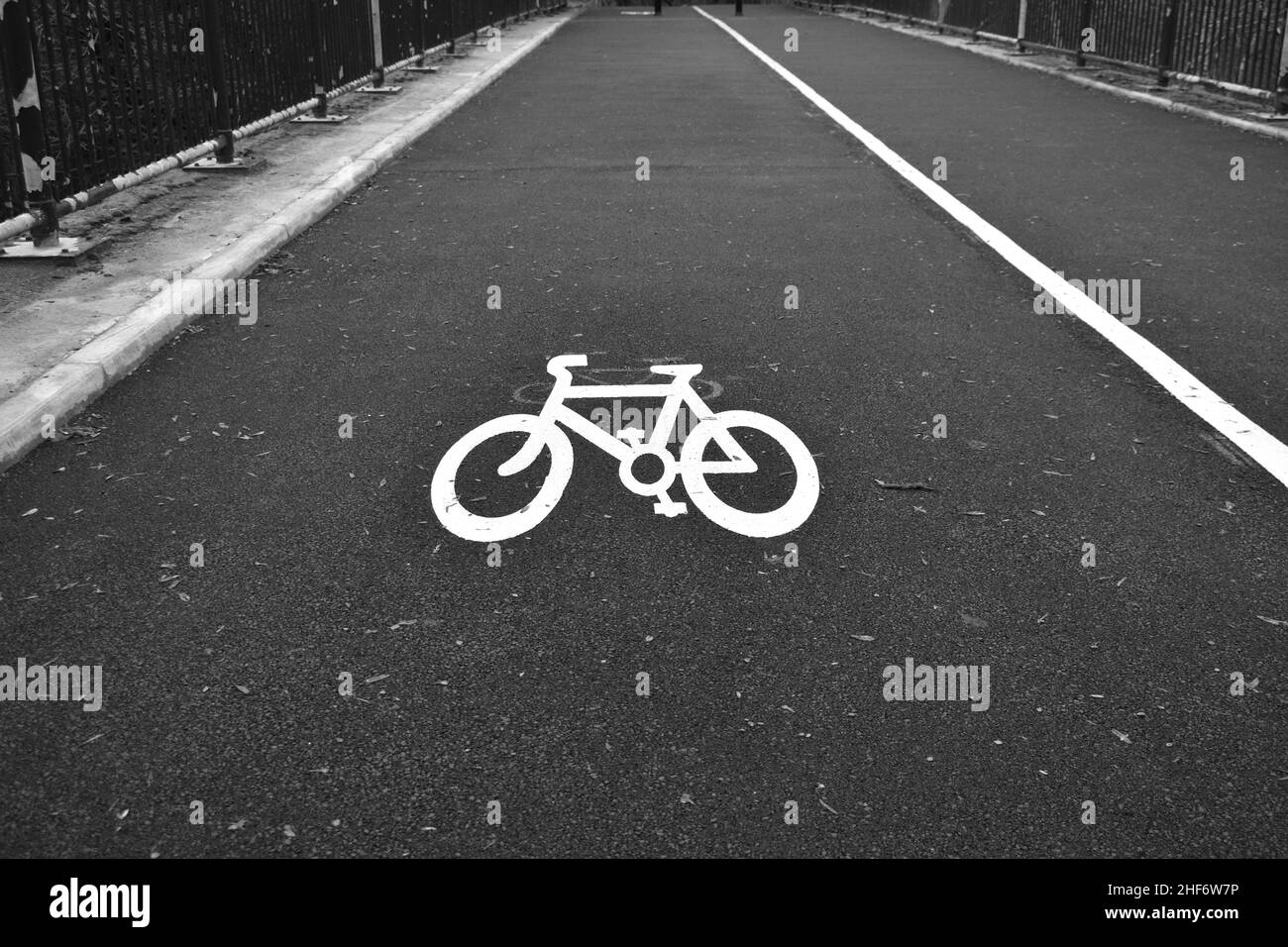 immagine di un simbolo di bicicletta bianco dipinto su asfalto nero all'esterno su una pista ciclabile con linee bianche che entrano in distanza con una prospettiva decrescente Foto Stock