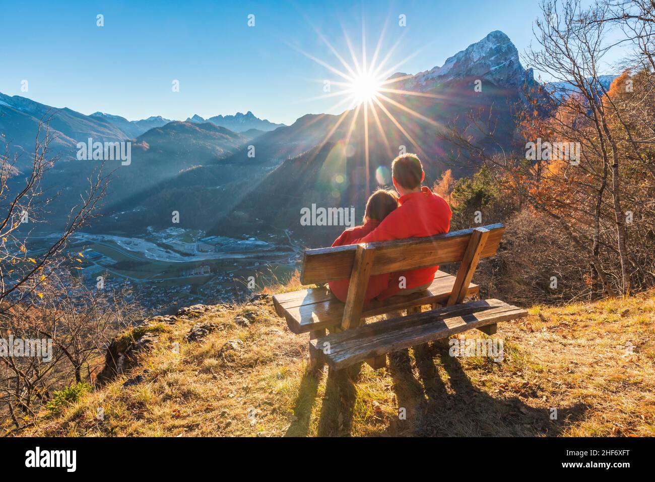 Due persone (padre e figlia) sedute su una panchina in autunno guardando il tramonto, Agordo, provincia Belluno, Veneto, Italia Foto Stock