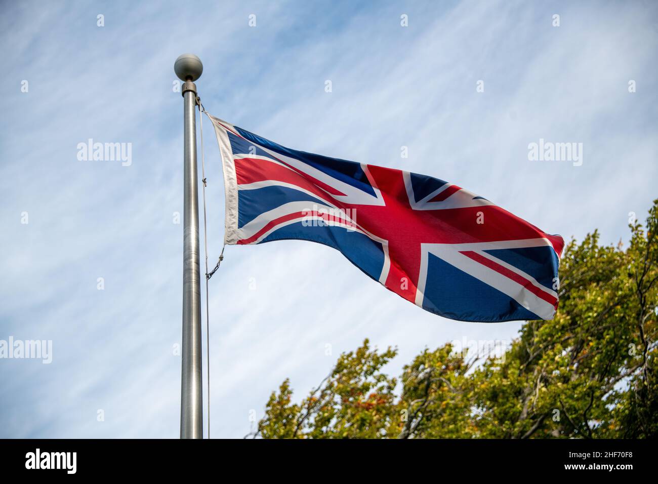 La bandiera europea è nota come Union Jack che vola su un palo di metallo con cielo blu e nuvole sullo sfondo. È una bandiera rossa, bianca e blu. Foto Stock