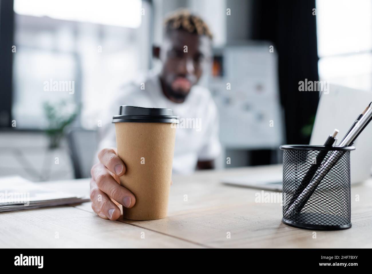 fuoco selettivo di bevanda di takeaway in mano dell'uomo afro-americano con pelle di vitiligine in ufficio Foto Stock