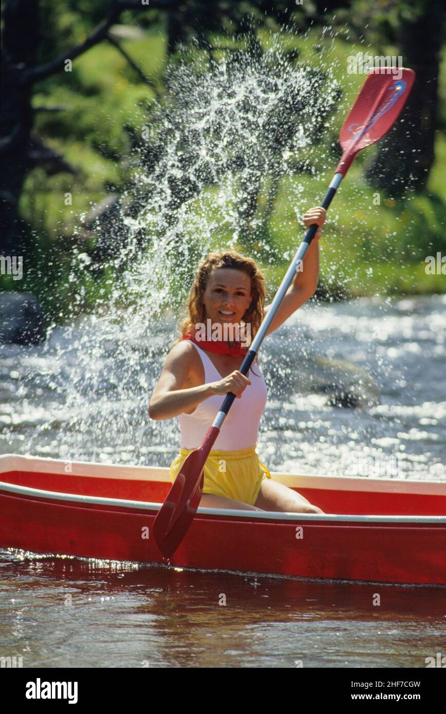 attraente bionda capelli sportive giovane donna pagaia sul canoo fiume freen fogliame sfondo paese all'aperto Foto Stock