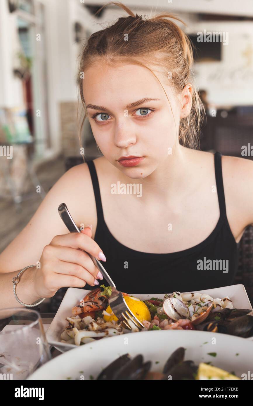 Giovane bella ragazza caucasica bionda mangia insalata di pesce in un ristorante mediterraneo Foto Stock