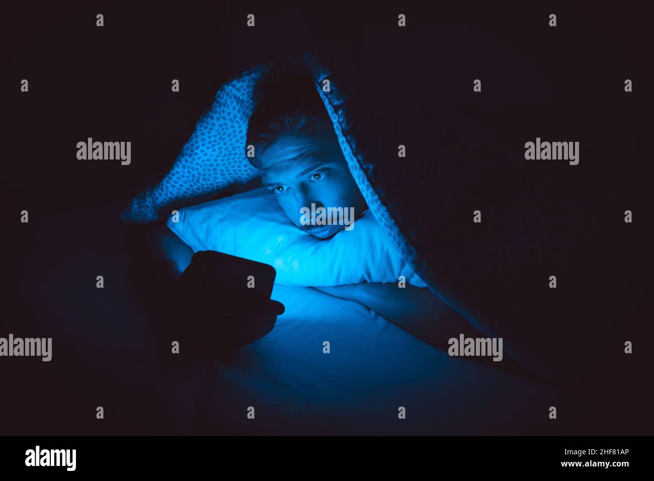 Giovane uomo sdraiato a letto e con smartphone prima di dormire. Dipendenza dai social media e insonnia Foto Stock