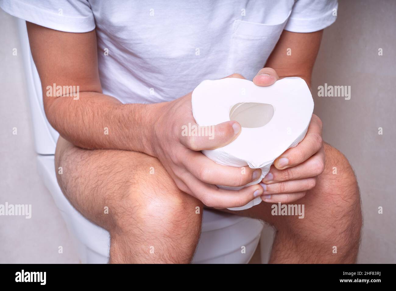 Uomo seduto sul gabinetto con carta igienica e che soffre di costipazione, diarrea, mal di stomaco o crampi Foto Stock