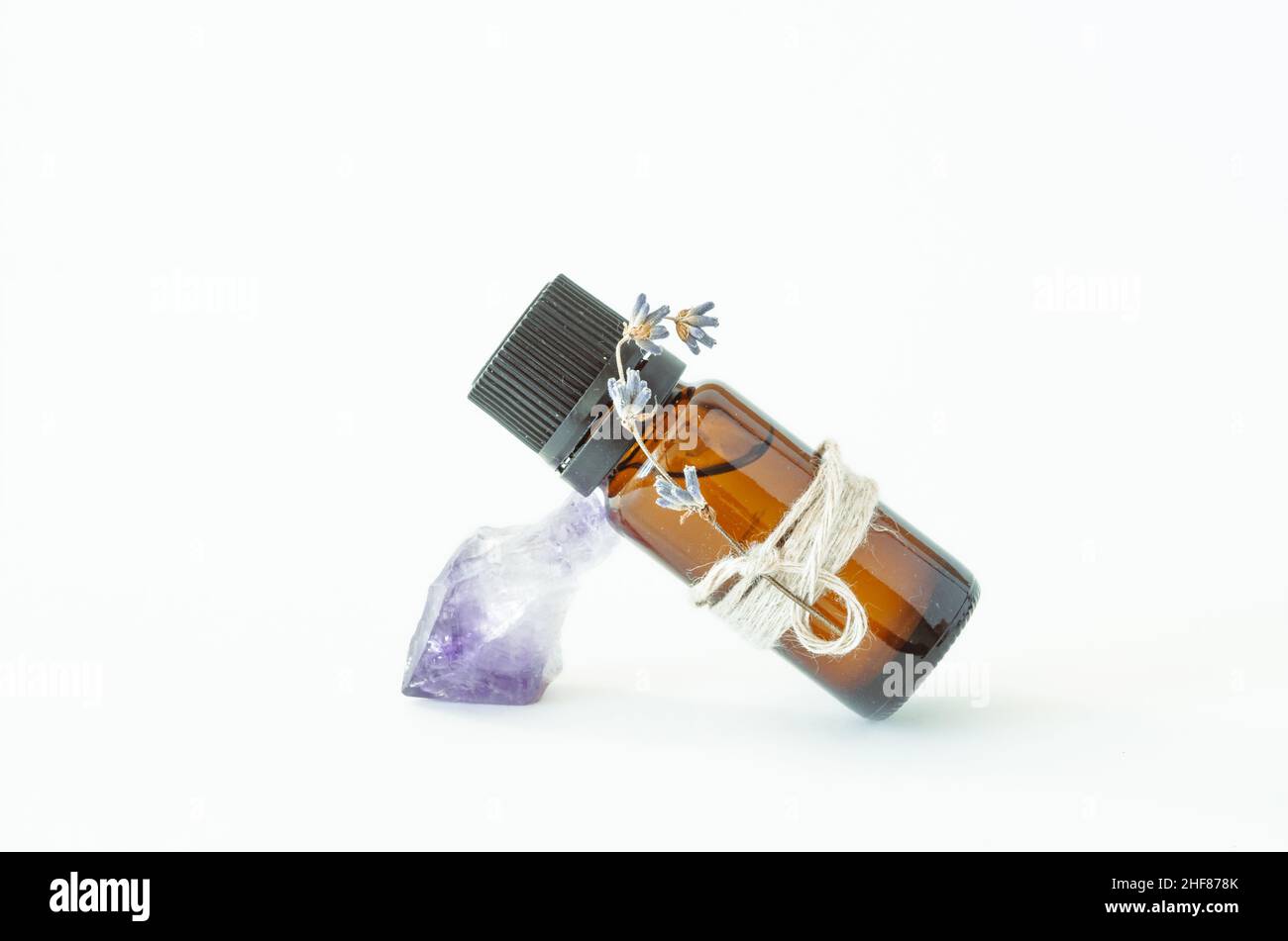 Bottiglia isolata di olio essenziale di lavanda appoggiata su cristallo viola di ametista su sfondo bianco Foto Stock