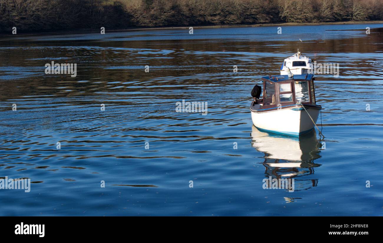 Piccole barche ormeggiate in un porto della Cornovaglia, acqua blu brillante con riflessi e ombre Foto Stock