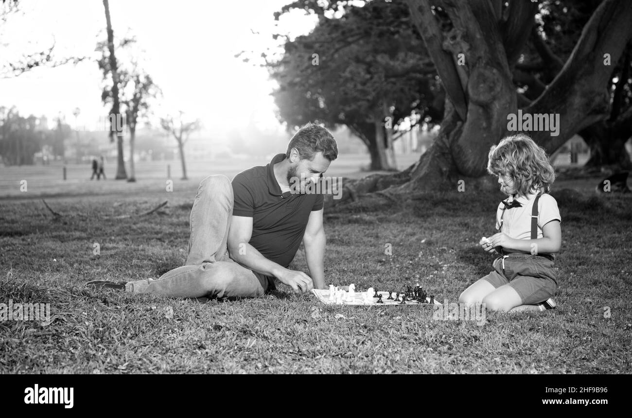 papà e bambino giocano un gioco di logica. padre e figlio giocano a scacchi sull'erba nel parco. giorno dei padri Foto Stock