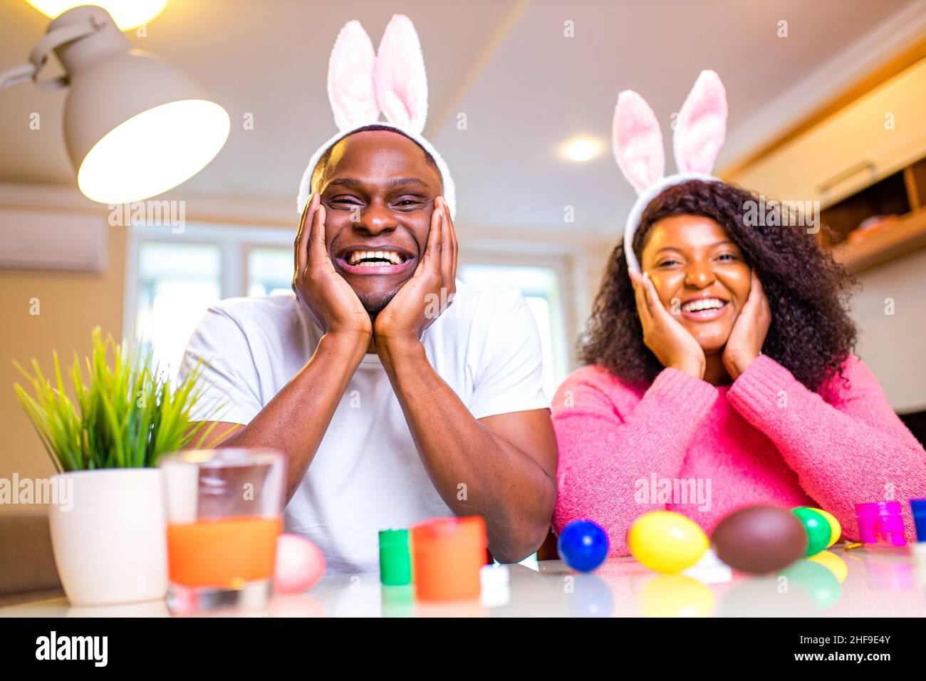 Giovane africano americano uomo e donna che indossa carino pasqua coniglietto orecchie e pittura uova in casa Foto Stock