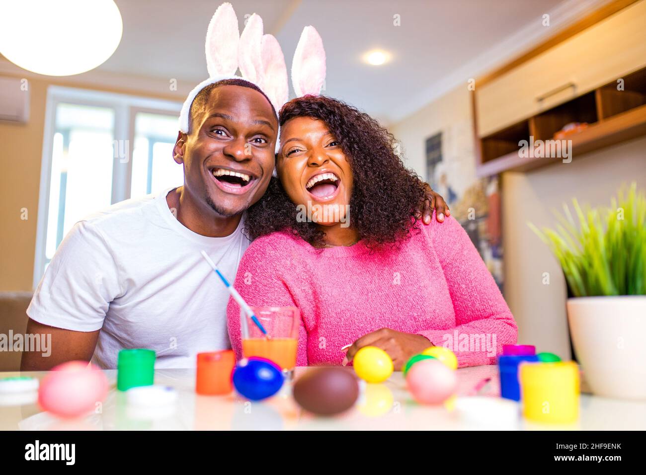 Giovane afroamericano uomo e donna persone autentiche che indossano graziose orecchie di coniglietto pasquale e dipingere uova in casa Foto Stock