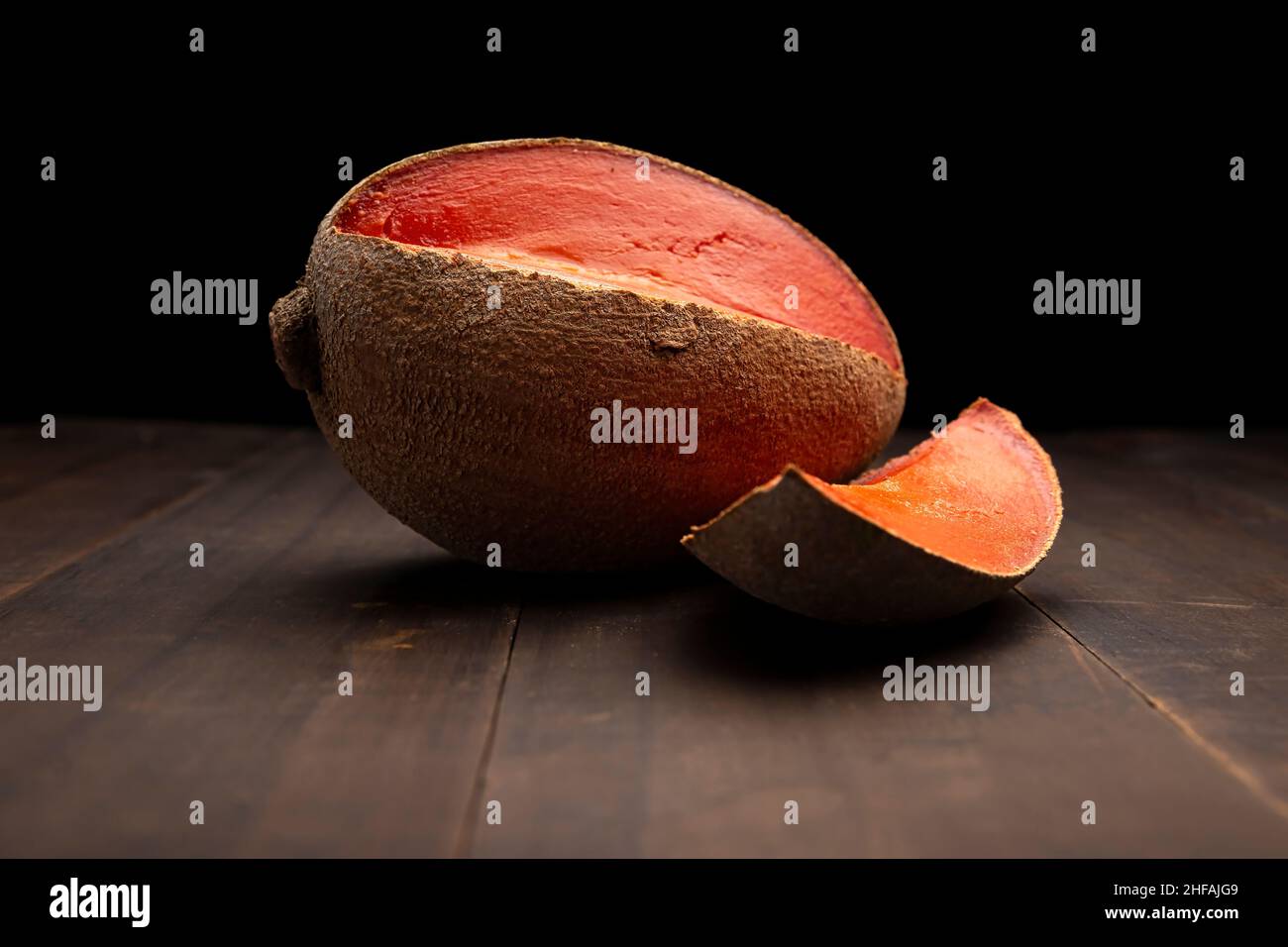 immagine di una mamey rossa messicana da vicino su superficie rustica in legno e sfondo nero Foto Stock