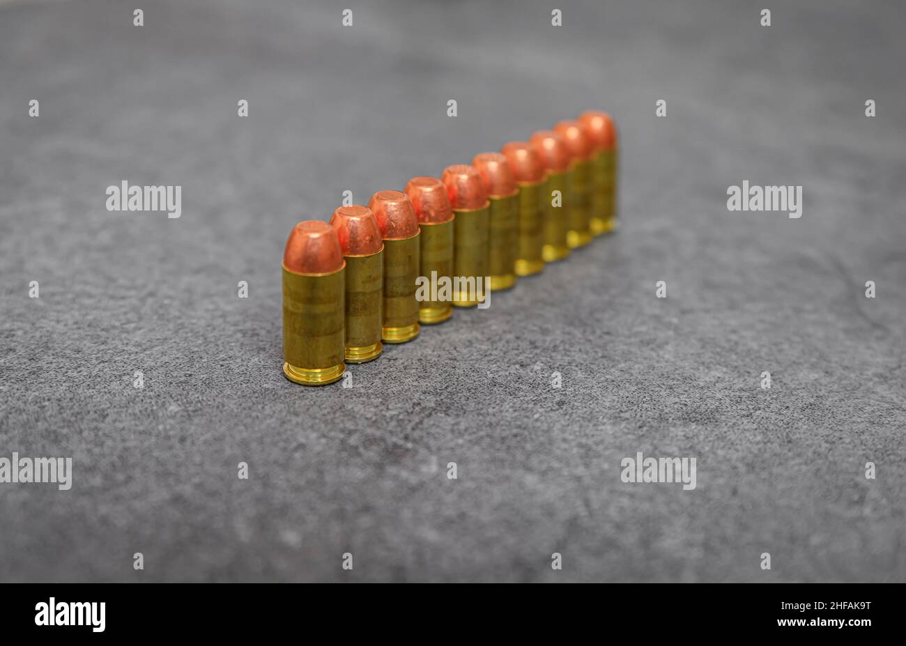 45 pallottole di rivestimento in metallo di calibro ACP sparate rotonde allineate su una superficie di pietra Foto Stock