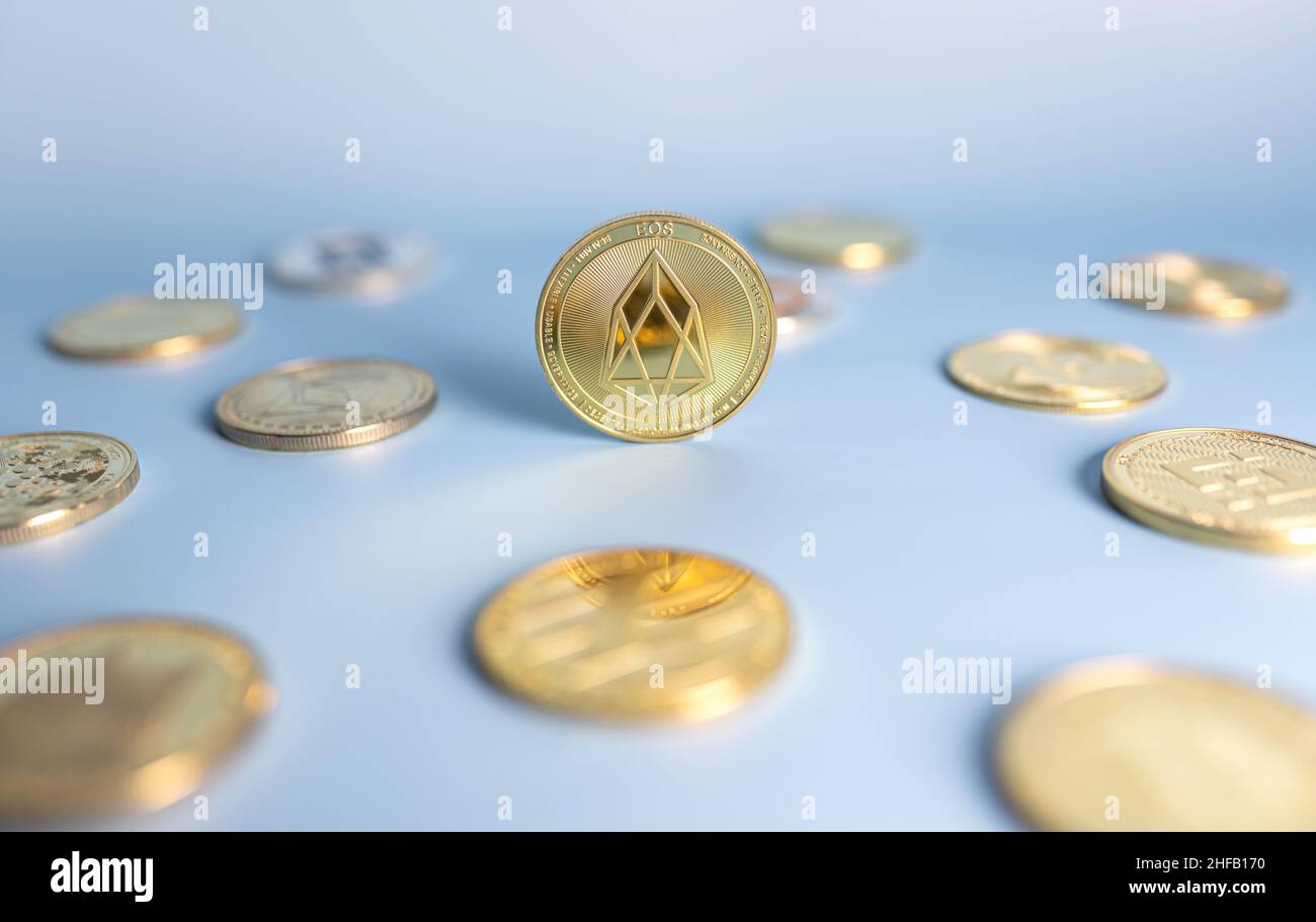 Moneta EOS in piedi in posizione centrale tra un mazzo di monete criptovaluta su sfondo blu. Banner con token EOSIO Crypto dorato. Primo piano, messa a fuoco morbida. Foto Stock