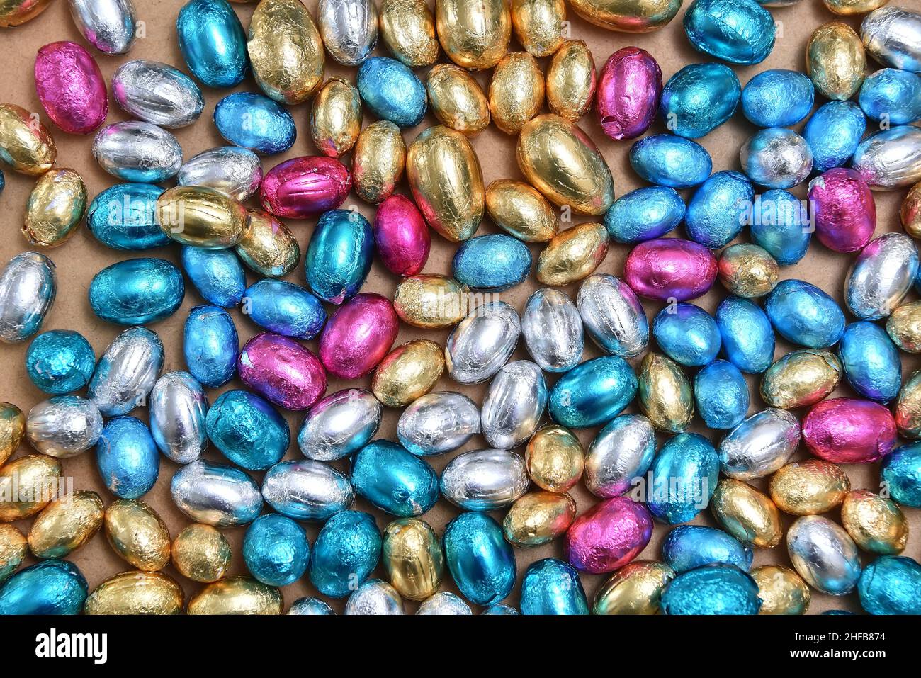 Un foglio grande e piccolo di colore rosa, blu, argento e oro avvolse le uova di pasqua al cioccolato su uno sfondo di legno chiaro. Foto Stock