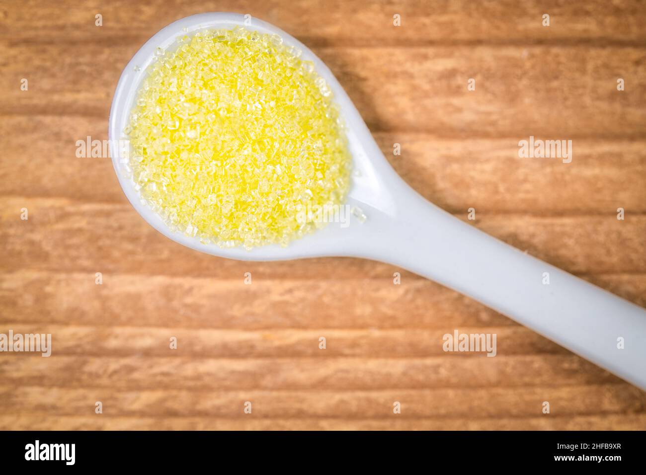 Zucchero giallo dolciario in un cucchiaio bianco Foto Stock