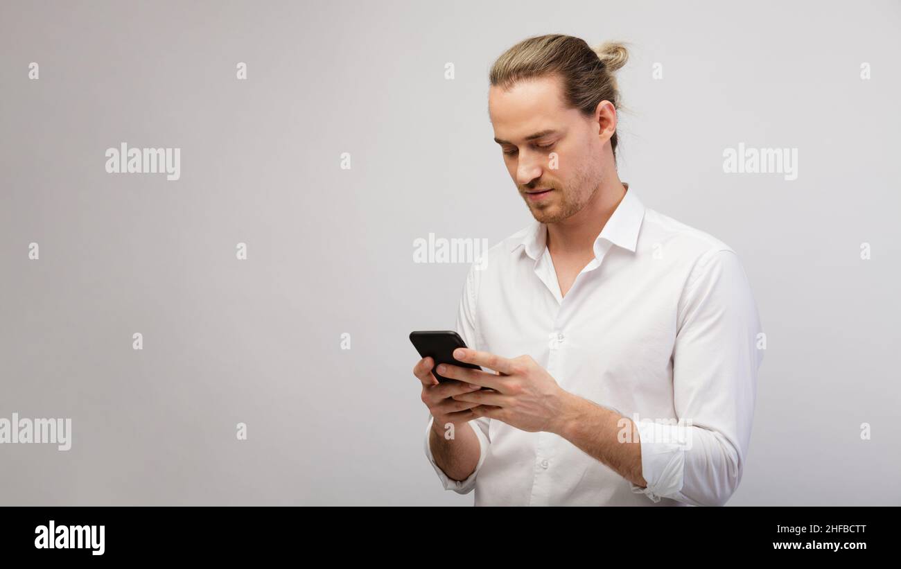 Giovane bionda bearded uomo che texting messaggio su smartphone su uno sfondo bianco studio con spazio copia Foto Stock