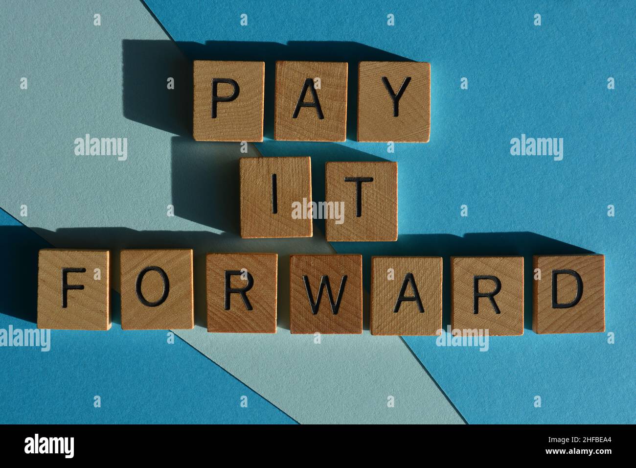 Pay it Forward, parole in lettere di legno di alfabeto isolato su sfondo blu Foto Stock