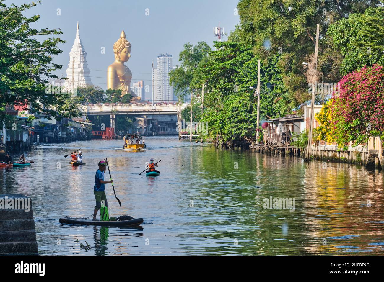 Giovani in canoa a Klong Bangkok Yai, un canale a Thonburi, Bangkok, Thailandia, Thonburi; b/g: Il Buddha gigante di Wat Paknam Phasi Charoen Foto Stock