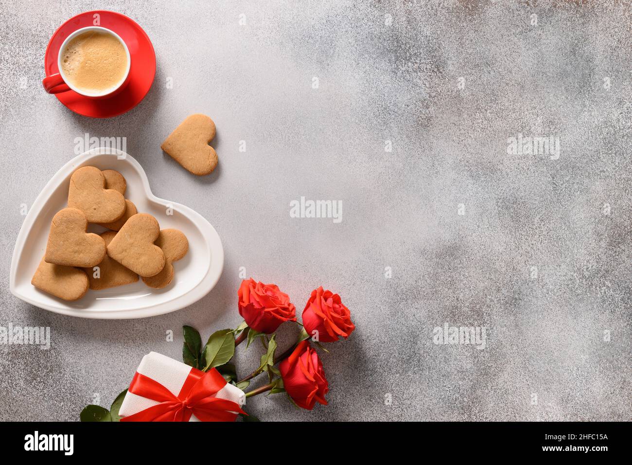 Caffè di San Valentino e biscotti a forma di cuore in piatto, bouquet di rose rosse e regalo d'amore. Vista dall'alto. Spazio di copia. Foto Stock
