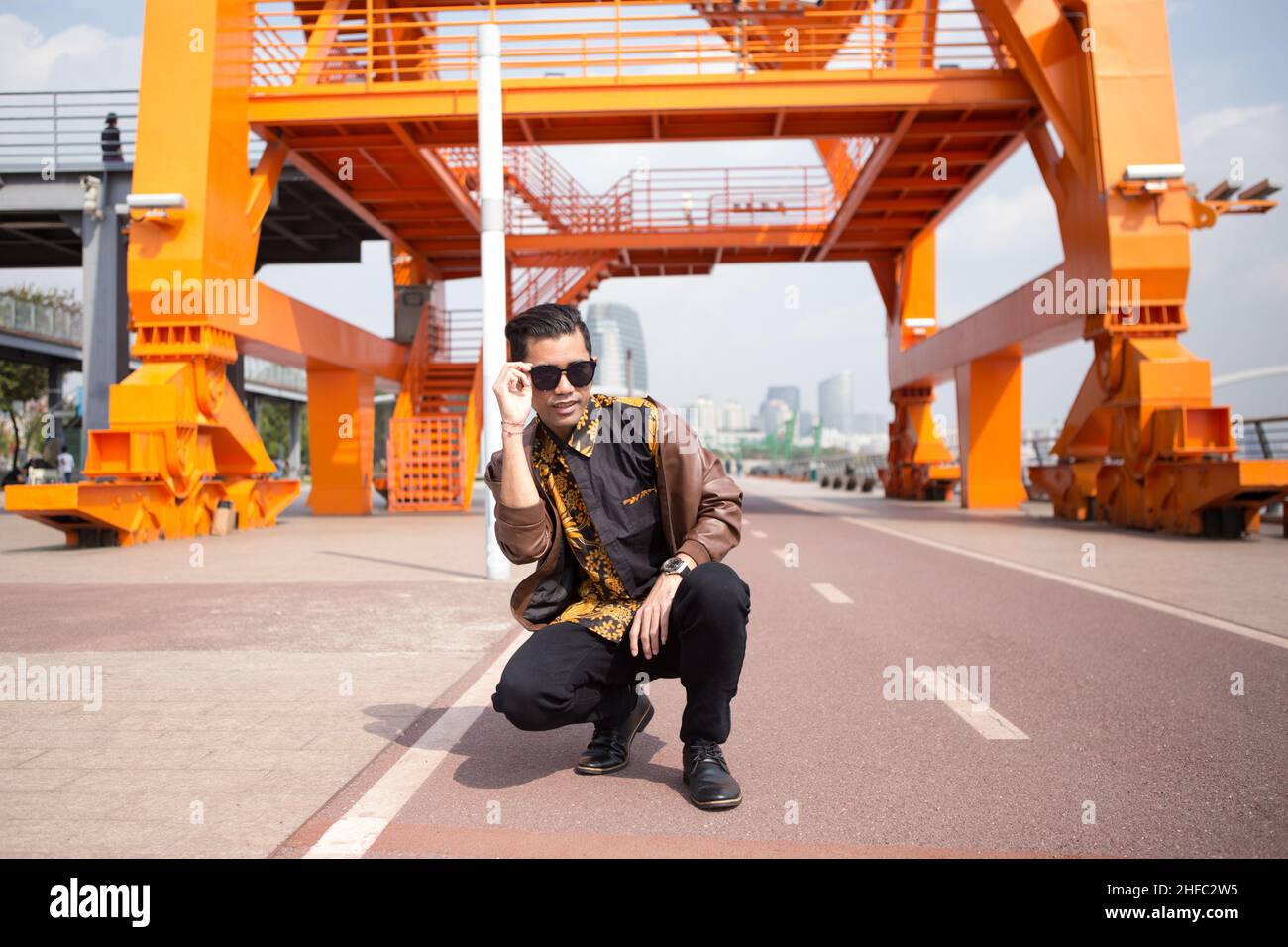 Un giovane modello maschile che indossa abiti batik indonesiani sotto una grande gru arancione al Long Museum, West Bund, Shanghai Cina Foto Stock