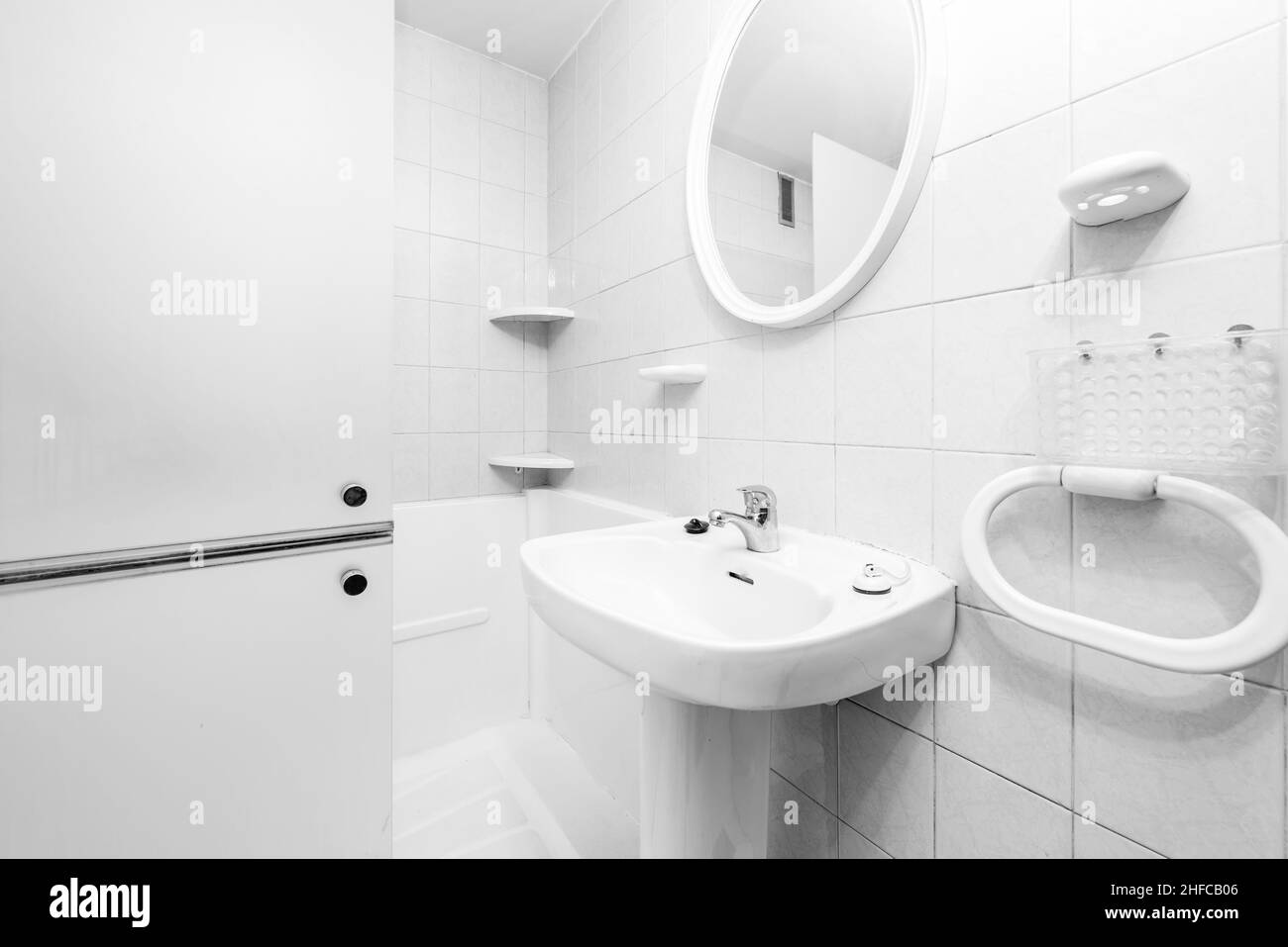 WC con armadietto bianco, lavandino in ceramica, portasciugamani e specchio circolare bianco con piastrelle bianche Foto Stock