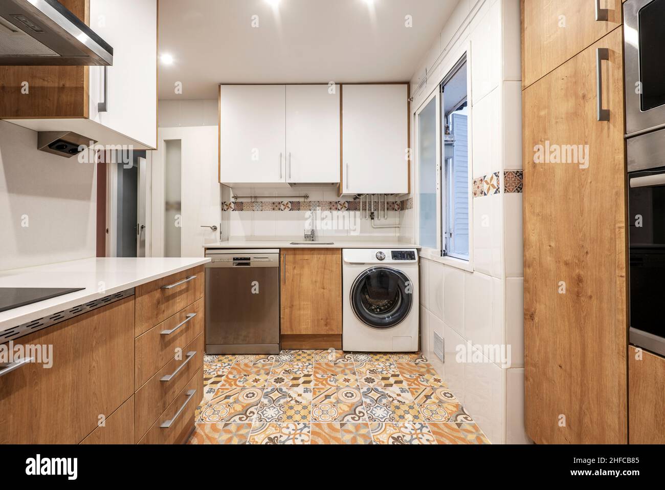 Cucina con mobili in legno combinati con mobili bianchi, pareti in porcellana bianca e pavimenti in gres idraulico Foto Stock