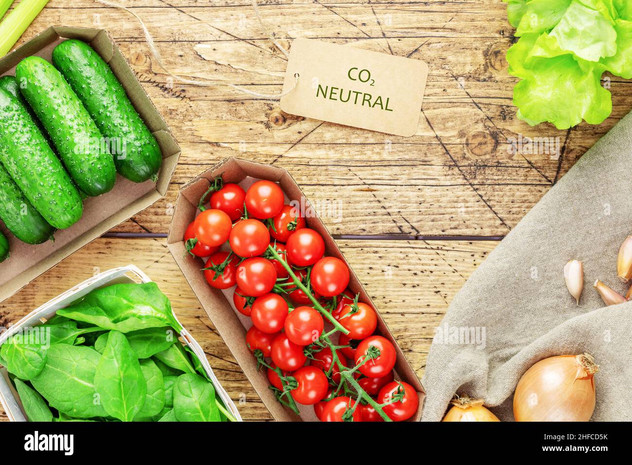 Composizione alimentare vegana sana con verdure locali, agricole in imballaggi eco-compatibili con un'etichetta con la scritta carbonio neutro su un dorso di legno Foto Stock