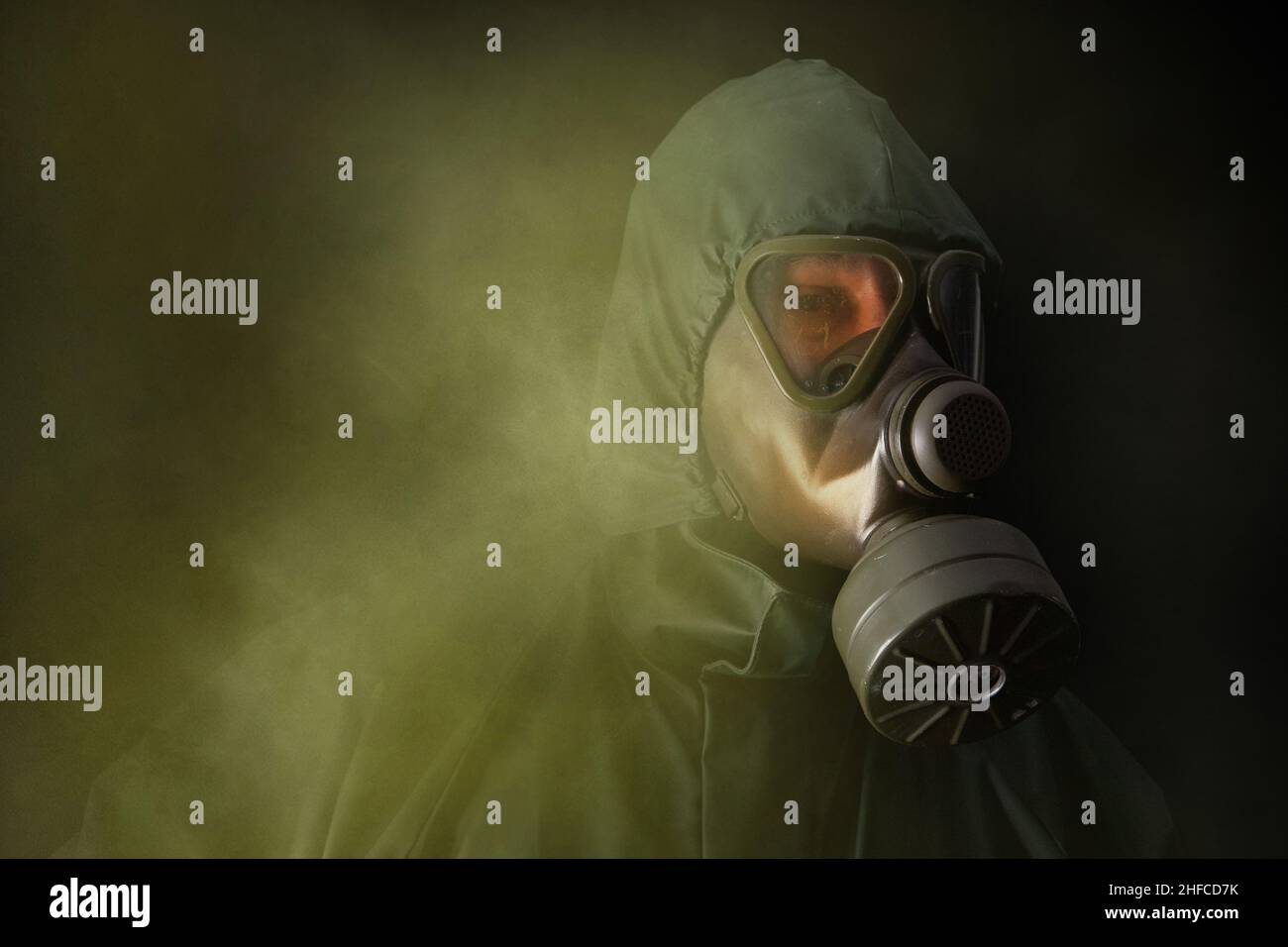 Un uomo in un vestito di protezione verde e maschera a gas cammina attraverso fumo tossico. Verticale a mezza lunghezza. Foto Stock