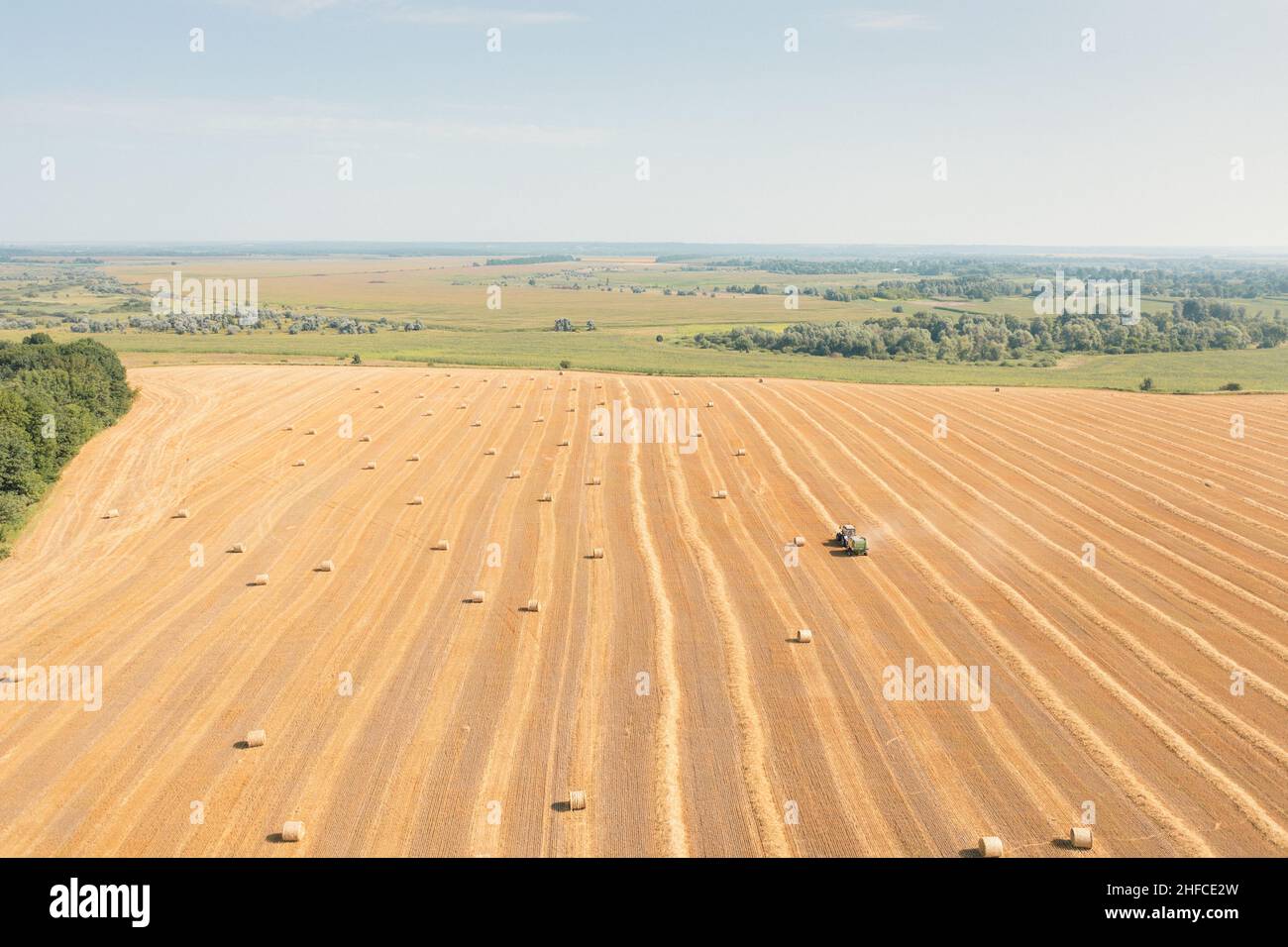 Produzione di balle di fieno con rotopressa di fieno con macchinari agricoli. Il trattore con rotopressa Hay lavora su balle di fieno raccolte su campo gialle: Colpo di vista con droni aerei. Foto Stock