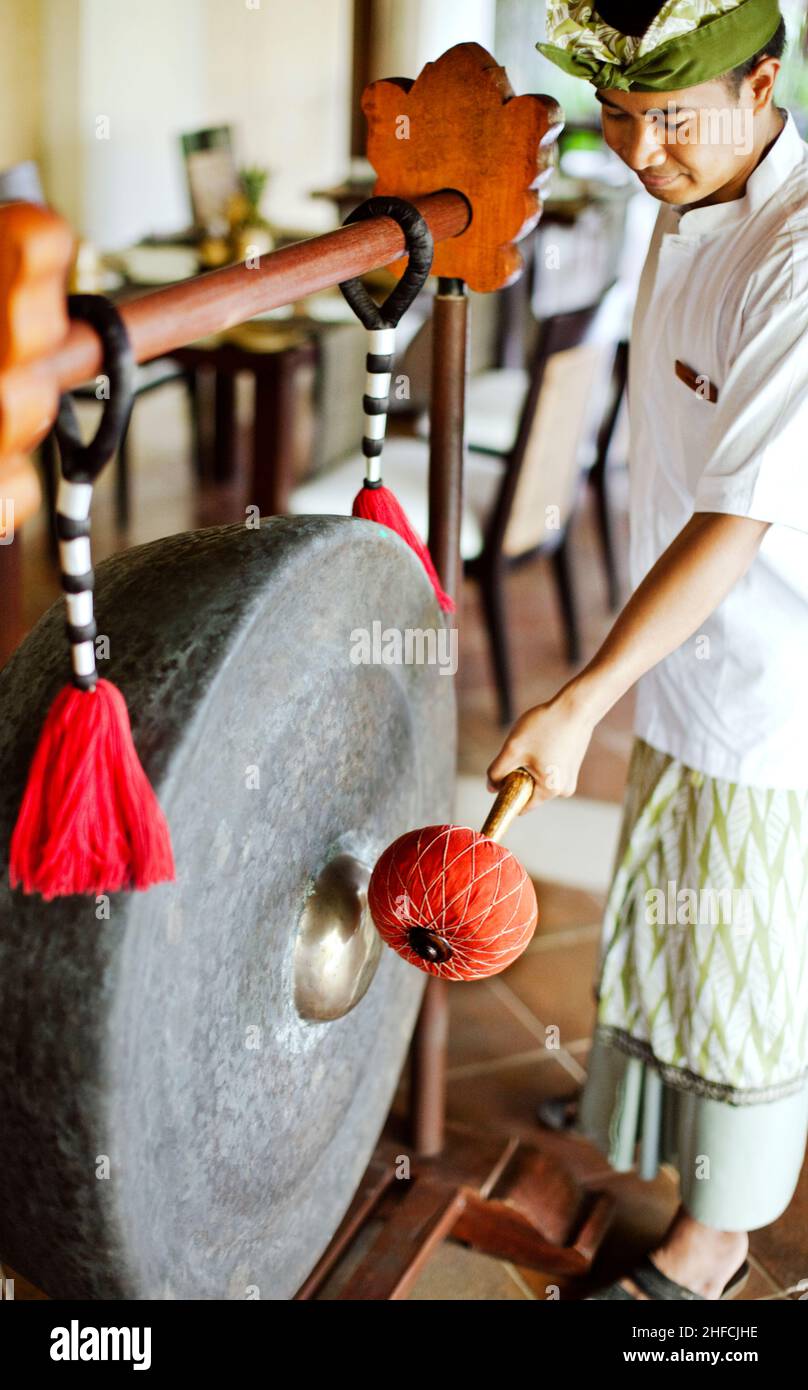 Il giovane cameriere balinese ha fatto un colpo di gong per accogliere gli ospiti al ristorante Gong, Kayumanis Gangsa, Bali, Indonesia. Foto Stock