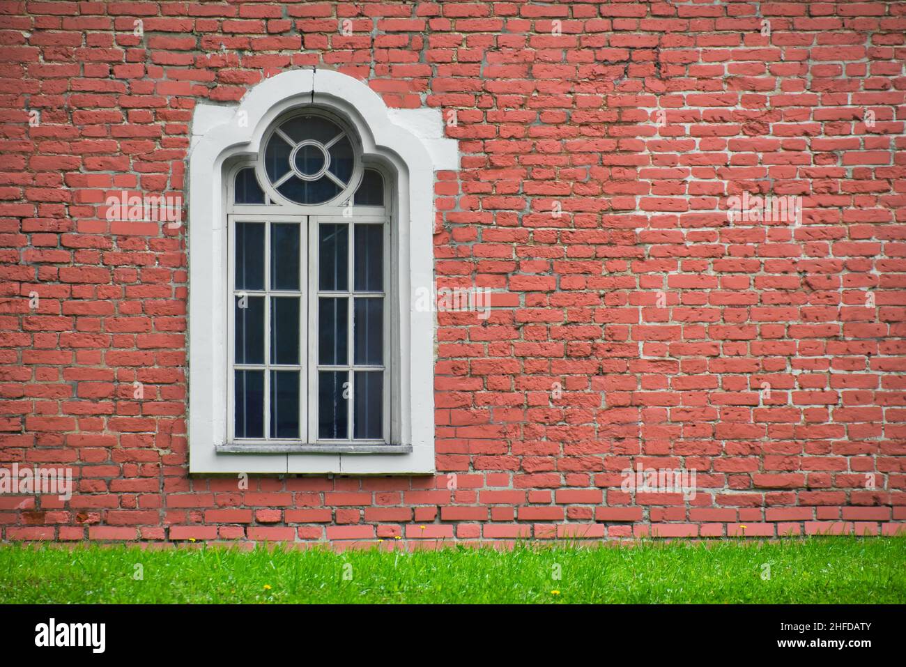 Muro di mattoni con una sola finestra fronte casa. Facciata di vecchio edificio e prato verde. Esterno di casa antica. Foto Stock