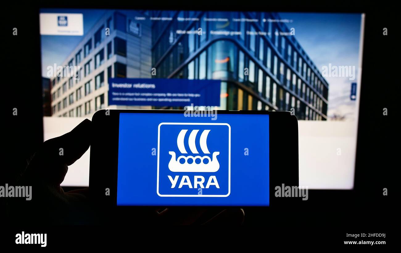 Persona che tiene il telefono cellulare con il logo della società chimica norvegese Yara International ASA sullo schermo di fronte alla pagina web. Mettere a fuoco sul display del telefono. Foto Stock