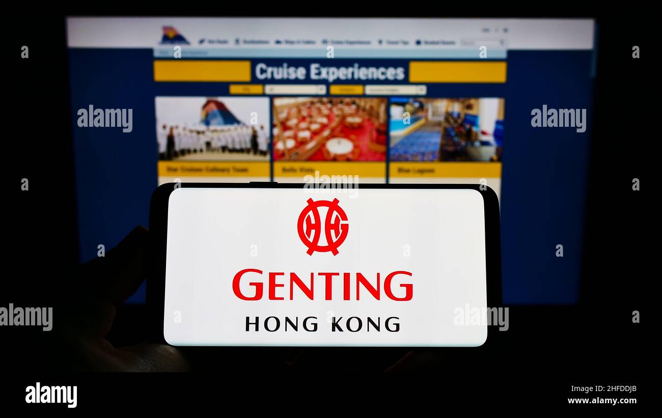 Persona che tiene il cellulare con il logo della società di turismo Genting Hong Kong sullo schermo di fronte alla pagina web Star Cruises. Mettere a fuoco sul display del telefono. Foto Stock