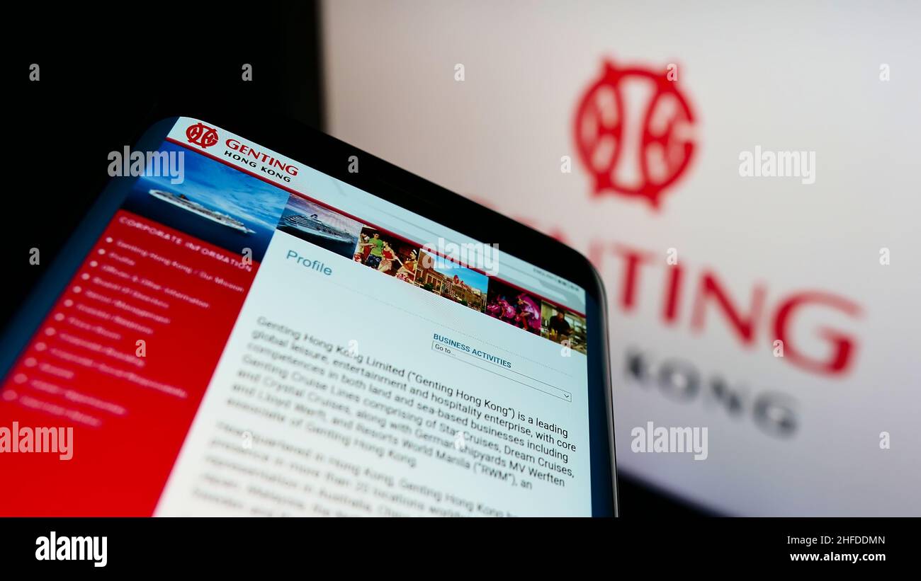 Telefono cellulare con sito web della società turistica Genting Hong Kong Limited sullo schermo di fronte al logo aziendale. Mettere a fuoco sulla parte superiore sinistra del display del telefono. Foto Stock