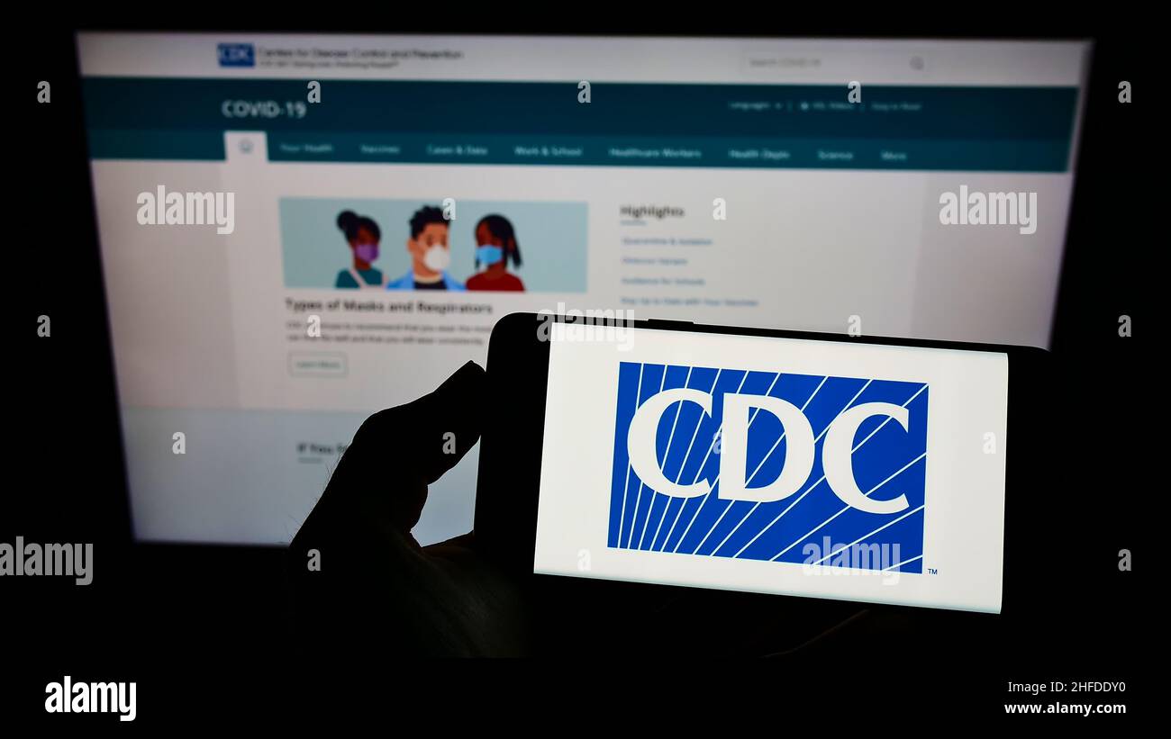 Persona che tiene uno smartphone con il logo del Centers for Disease Control and Prevention (CDC) sullo schermo di fronte al sito Web. Mettere a fuoco sul display del telefono. Foto Stock