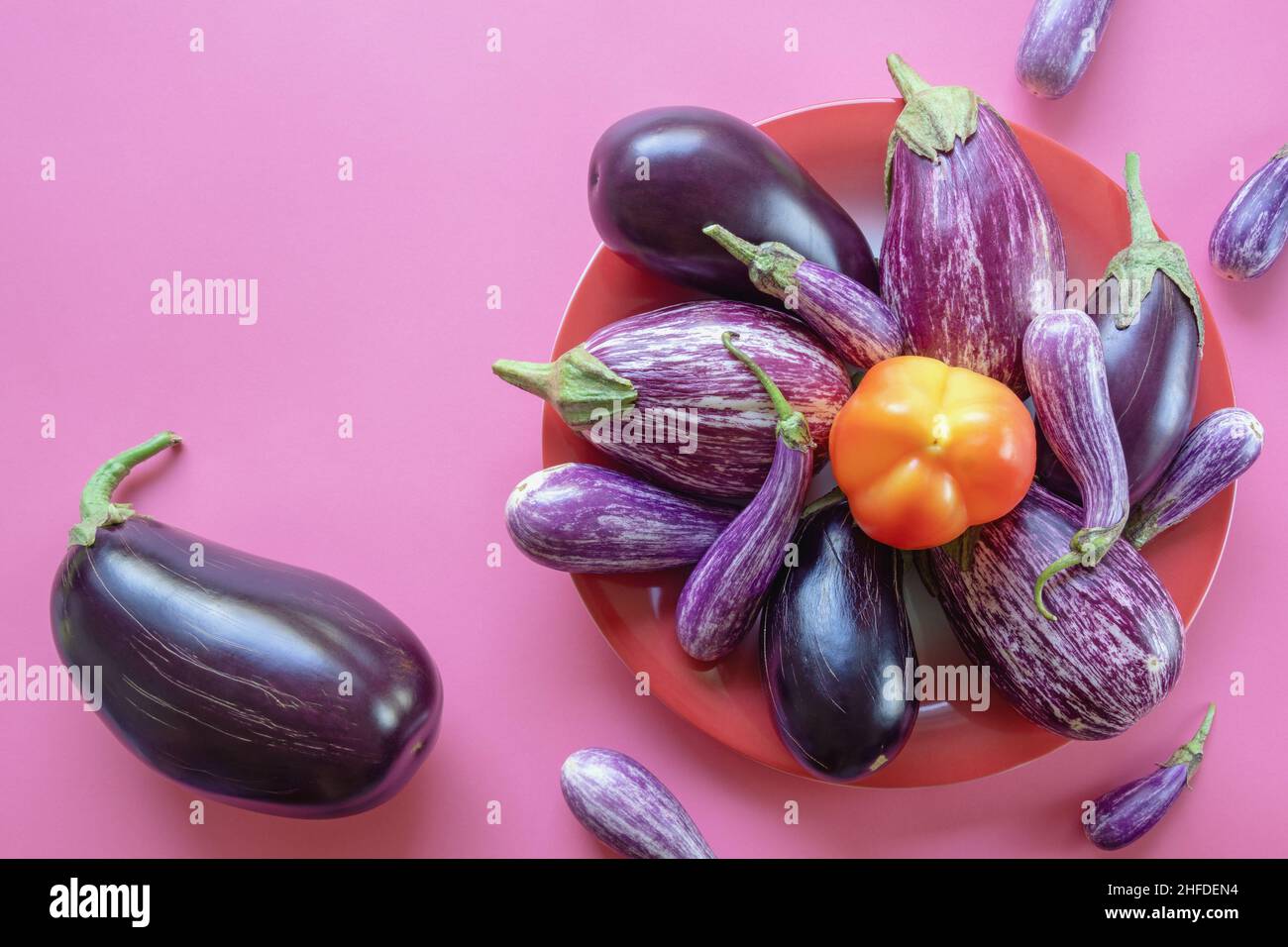 Verdure. Peperone e diverse melanzane in piatto rosso su sfondo rosa. Concetti di cibo sano e vegetariano. Spazio libero per il testo Foto Stock