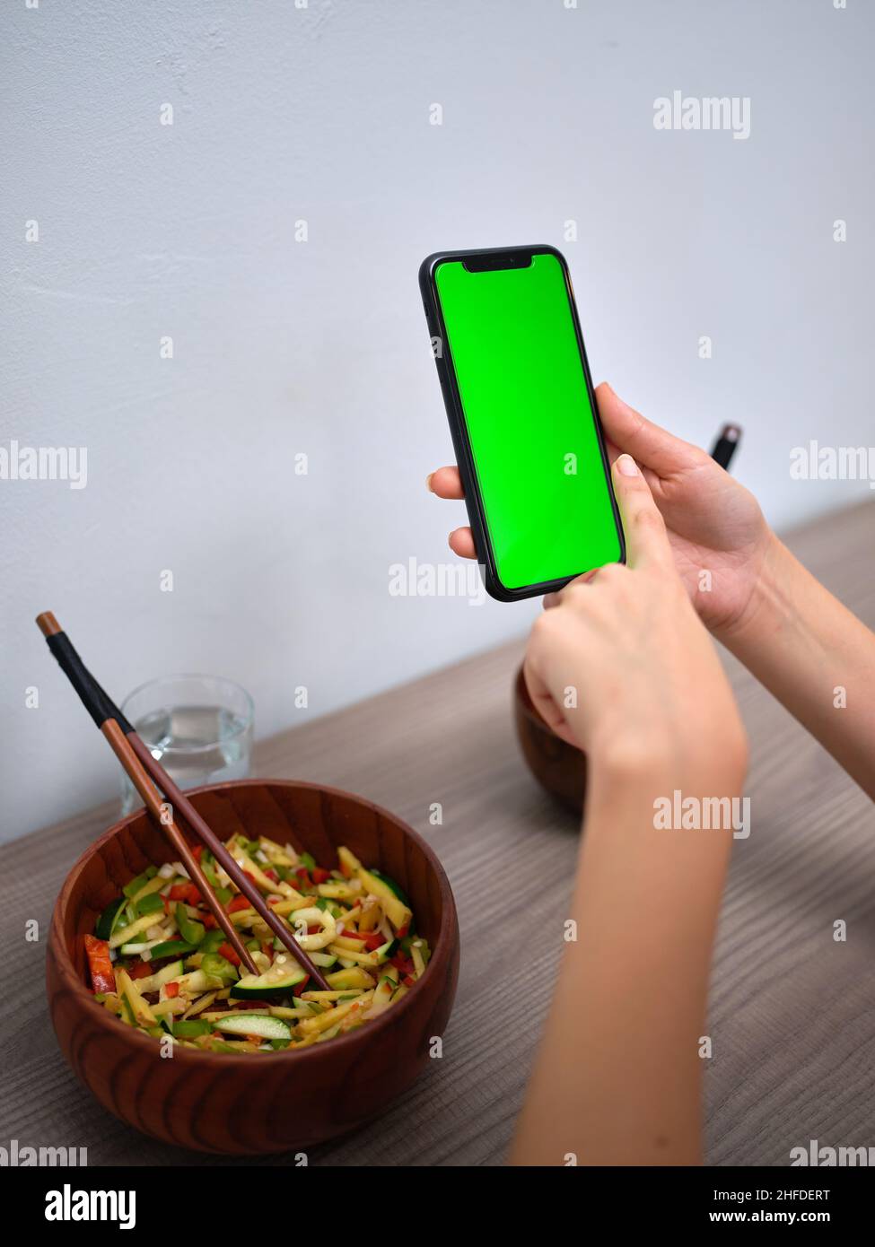 ciotola di verdure con bacchette, e le mani puntano verso lo schermo verde di un telefono Foto Stock