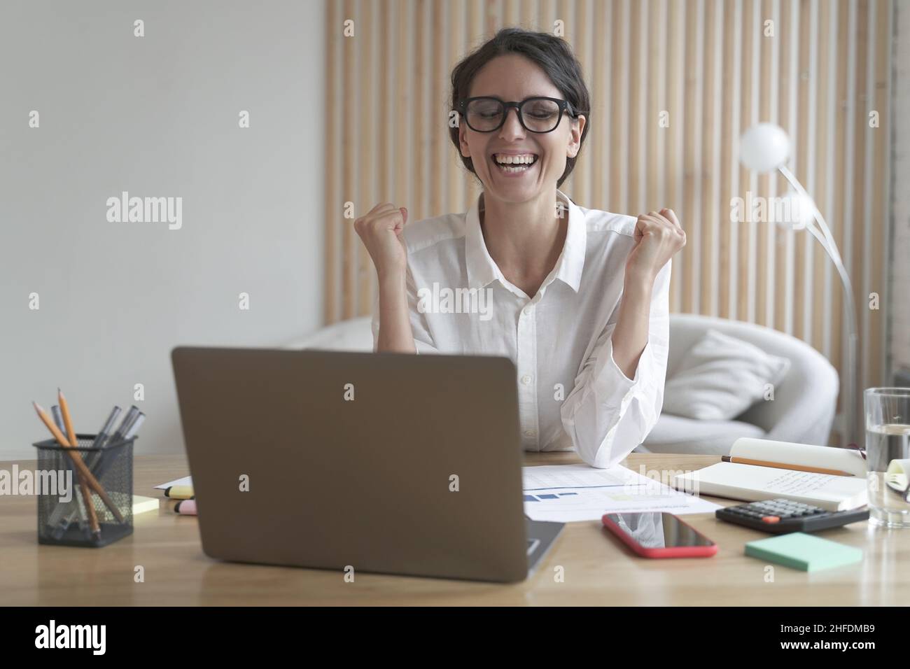 Eccitata dipendente femminile in occhiali che celebrano il successo o buoni risultati di lavoro Foto Stock