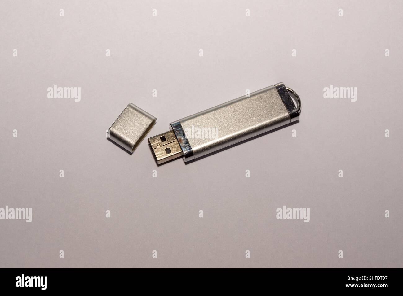 Un'unità flash USB argentata con un cappuccio aperto, abbastanza utilizzata con un rivestimento del contenitore usurato, si trova su una superficie bianca, messa a fuoco selettiva Foto Stock