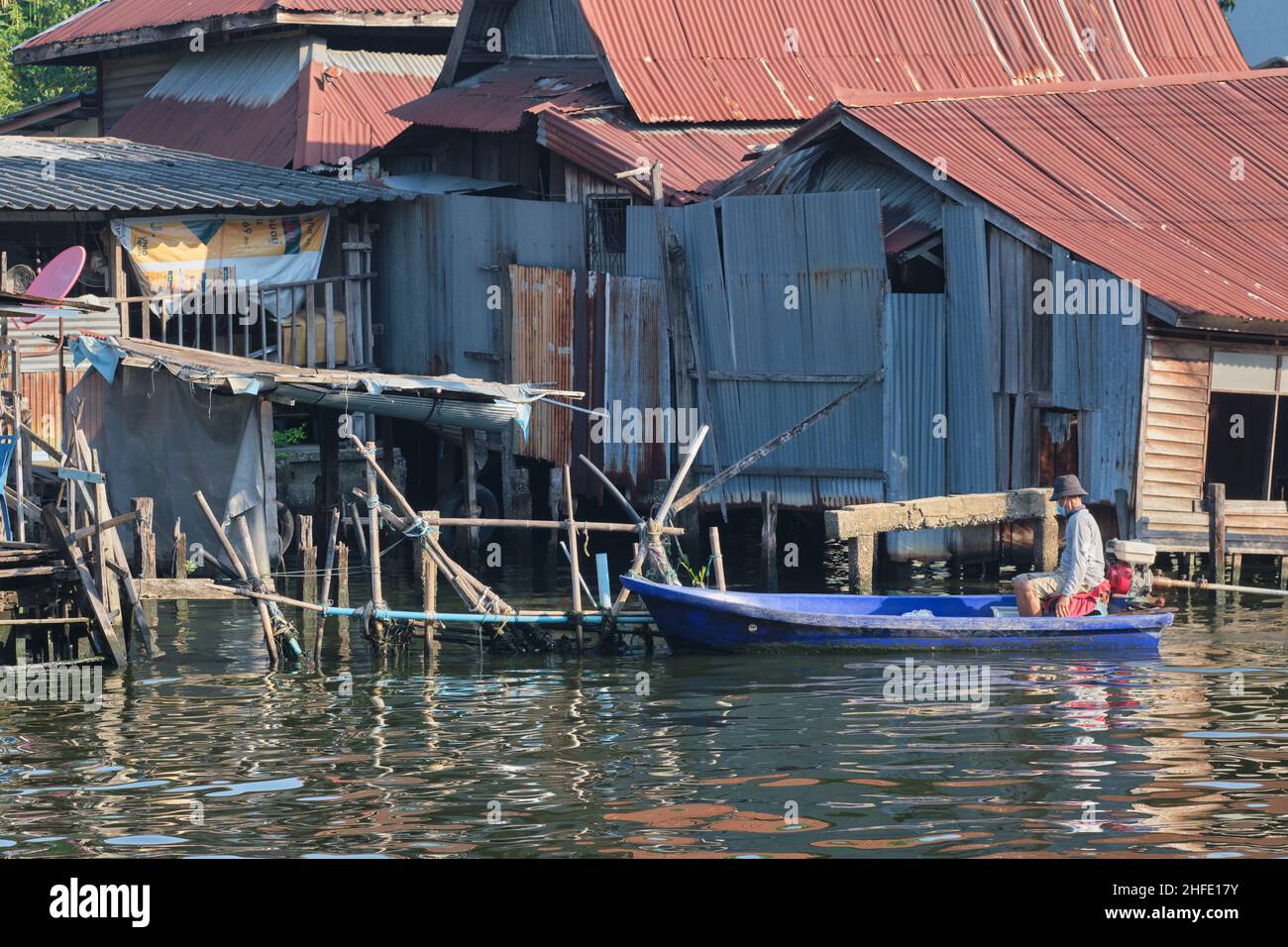 Un uomo guida la sua barca a Klong Bangkok Yai, un canale importante a Thonburi, Bangkok, Thailandia, passando attraverso le povere abitazioni lungo il bordo del canale Foto Stock