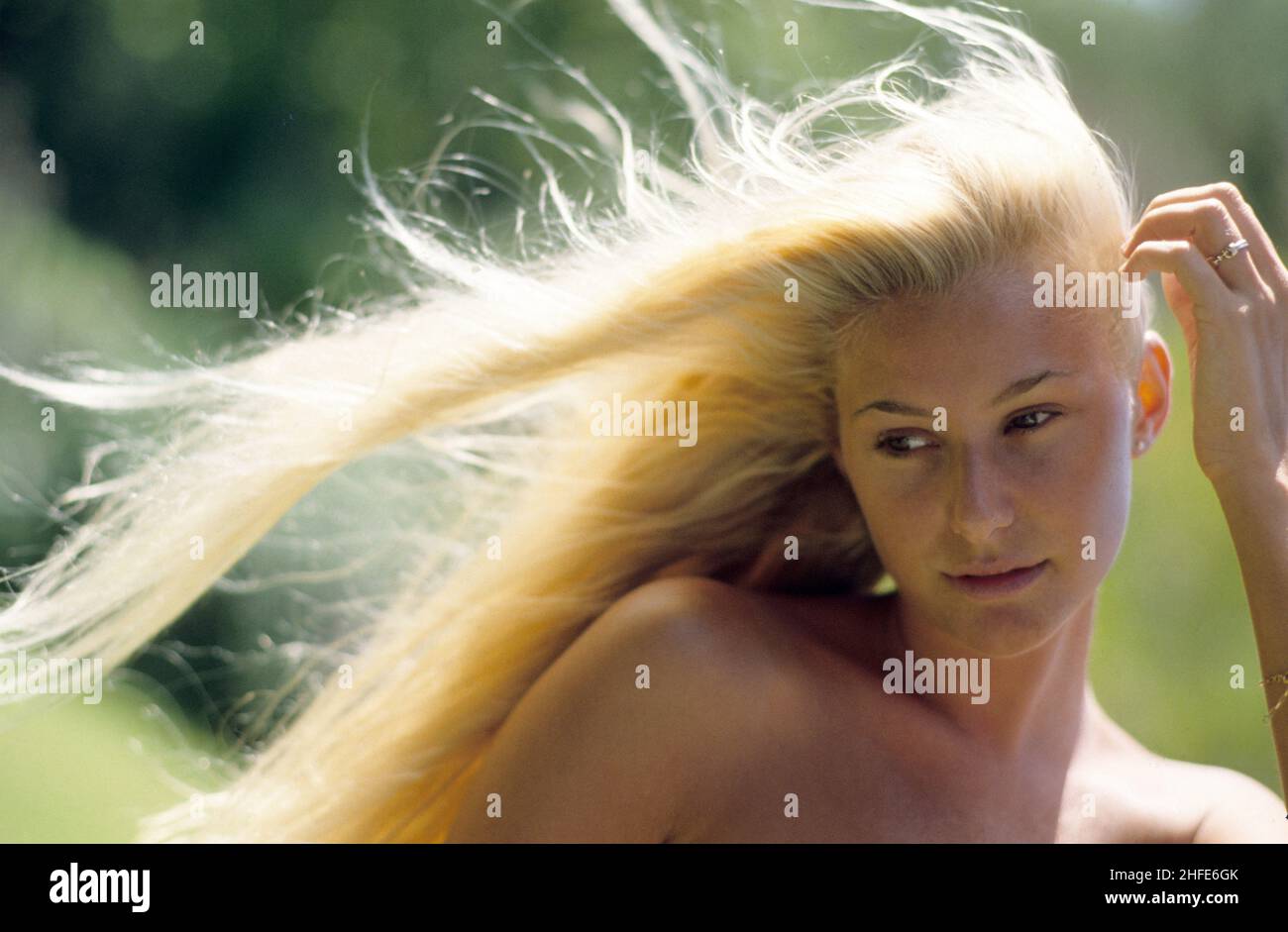 capelli biondi giovane ragazza profilo espressivo corpo gettando capelli spruzzi cielo blu e sfondo di acqua di mare Foto Stock
