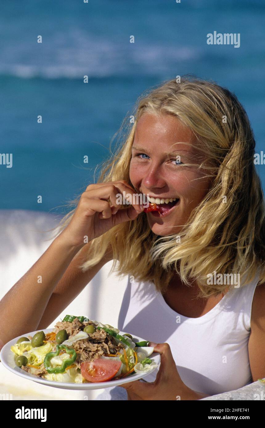 capelli biondi giovane donna ritratto bianco gonna naturale guardare fotocamera mangiare insalata piatto Foto Stock