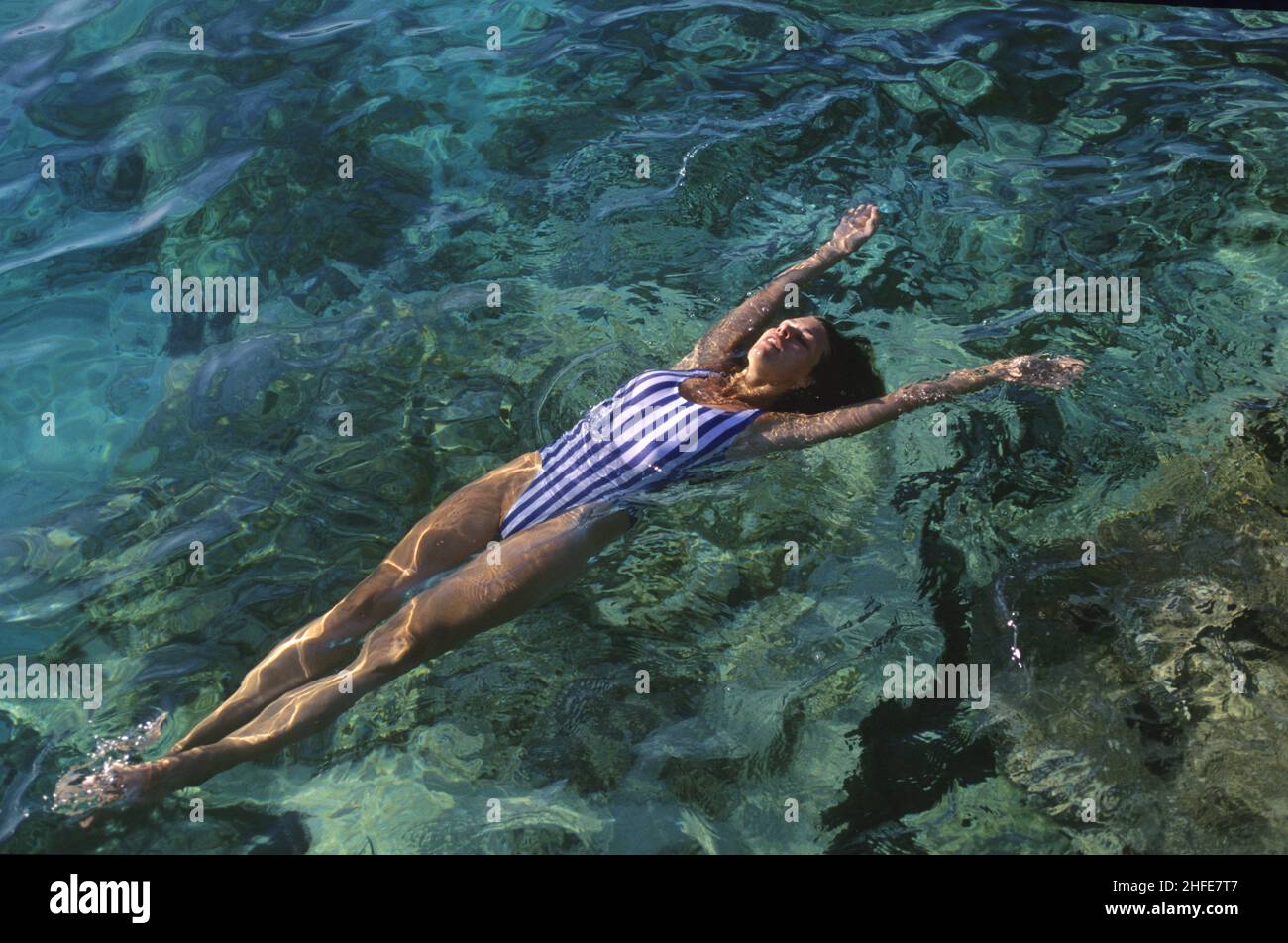 capelli scuri giovane donna sirena swimming indietro rilassante corpo galleggiante acqua di mare luce naturale Foto Stock