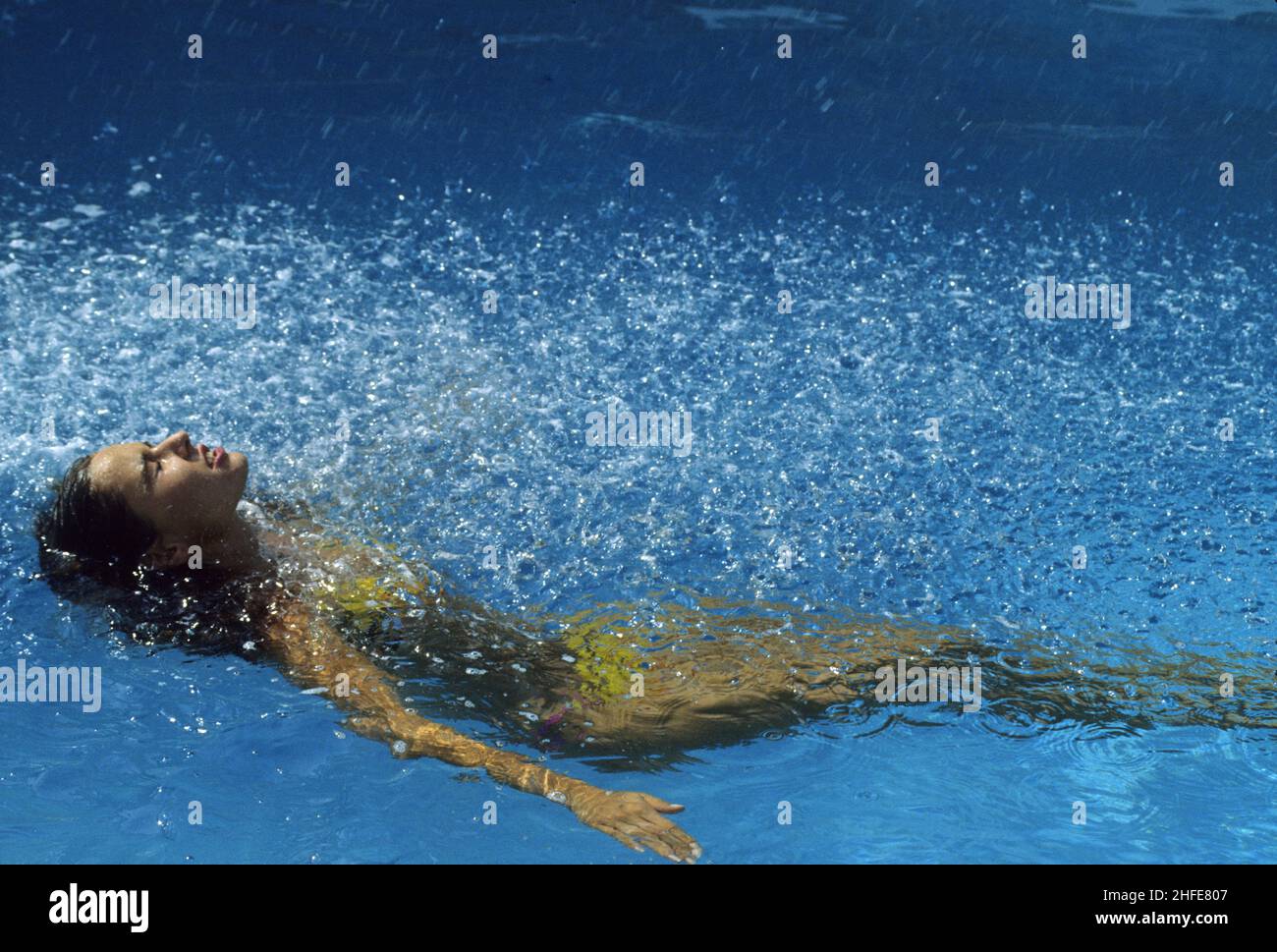capelli blrown giovane donna profilo vista acqua jet blu acqua piscina sfondo sorriso viso con spruzzi Foto Stock