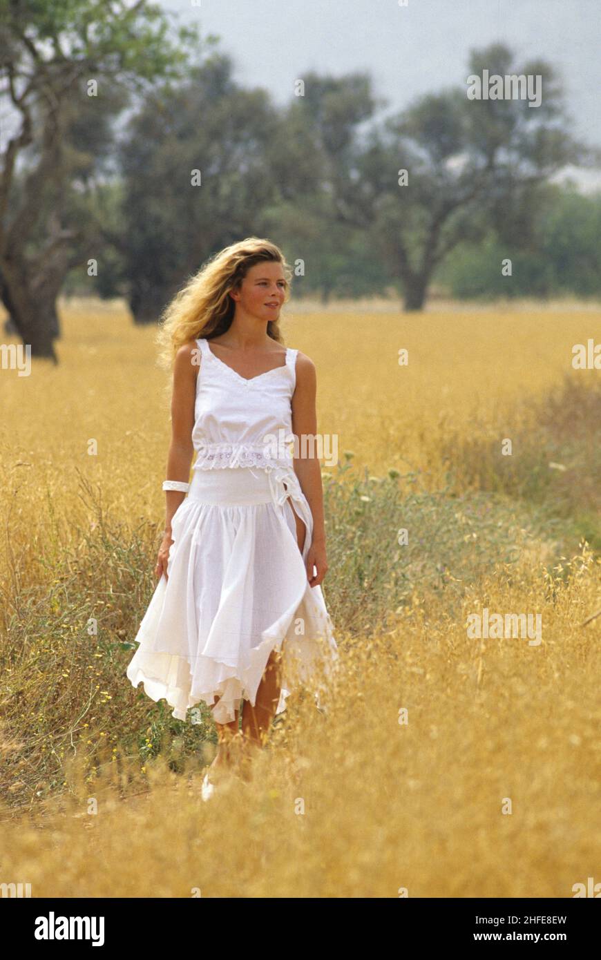 bella bionda capelli giovane ragazza molto romantica a piedi davanti la macchina fotografica bianco vestito giallo erbe sfondo paese Foto Stock